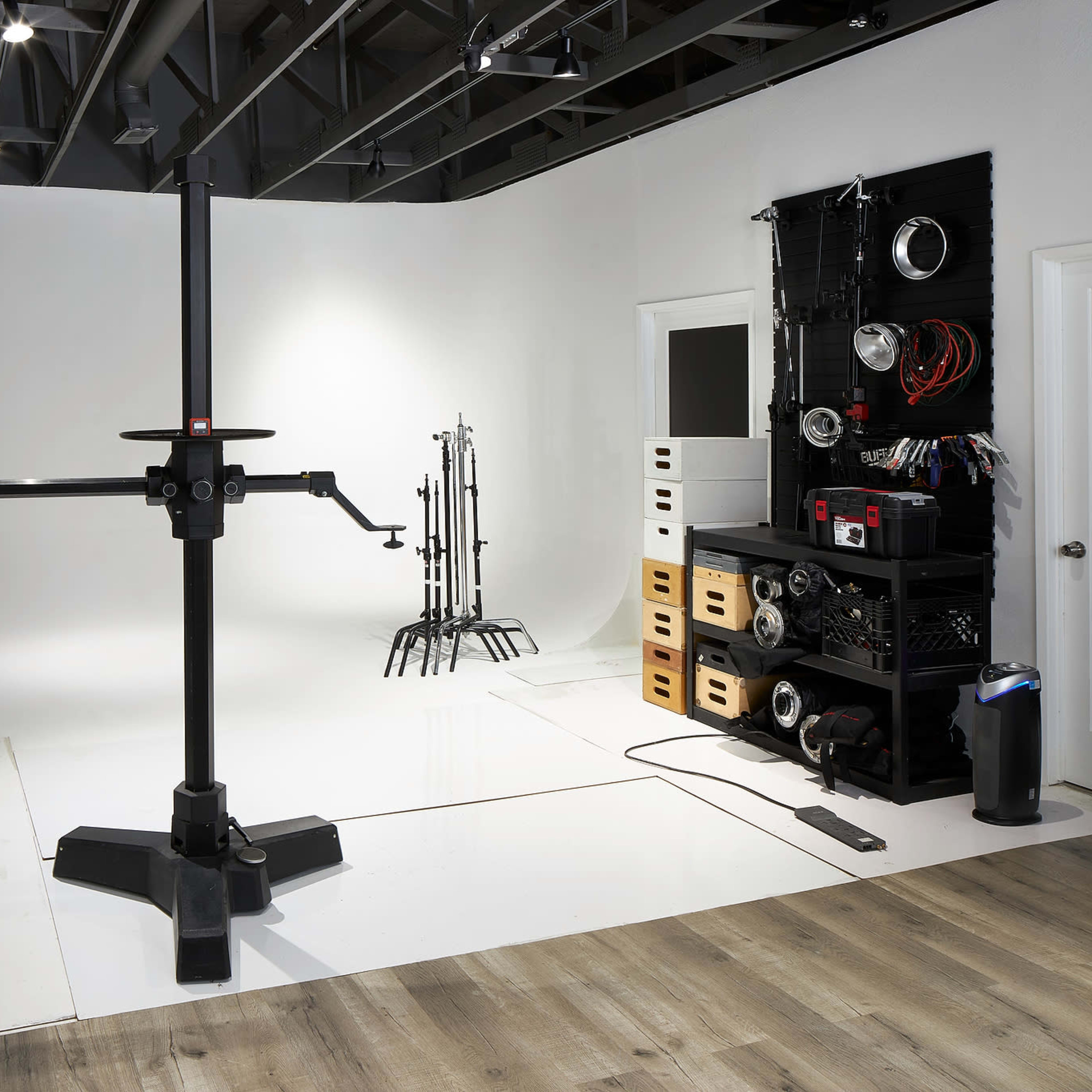 A photography studio with a central tripod, various light stands, backdrop support, and organizational furniture for equipment along the wall.