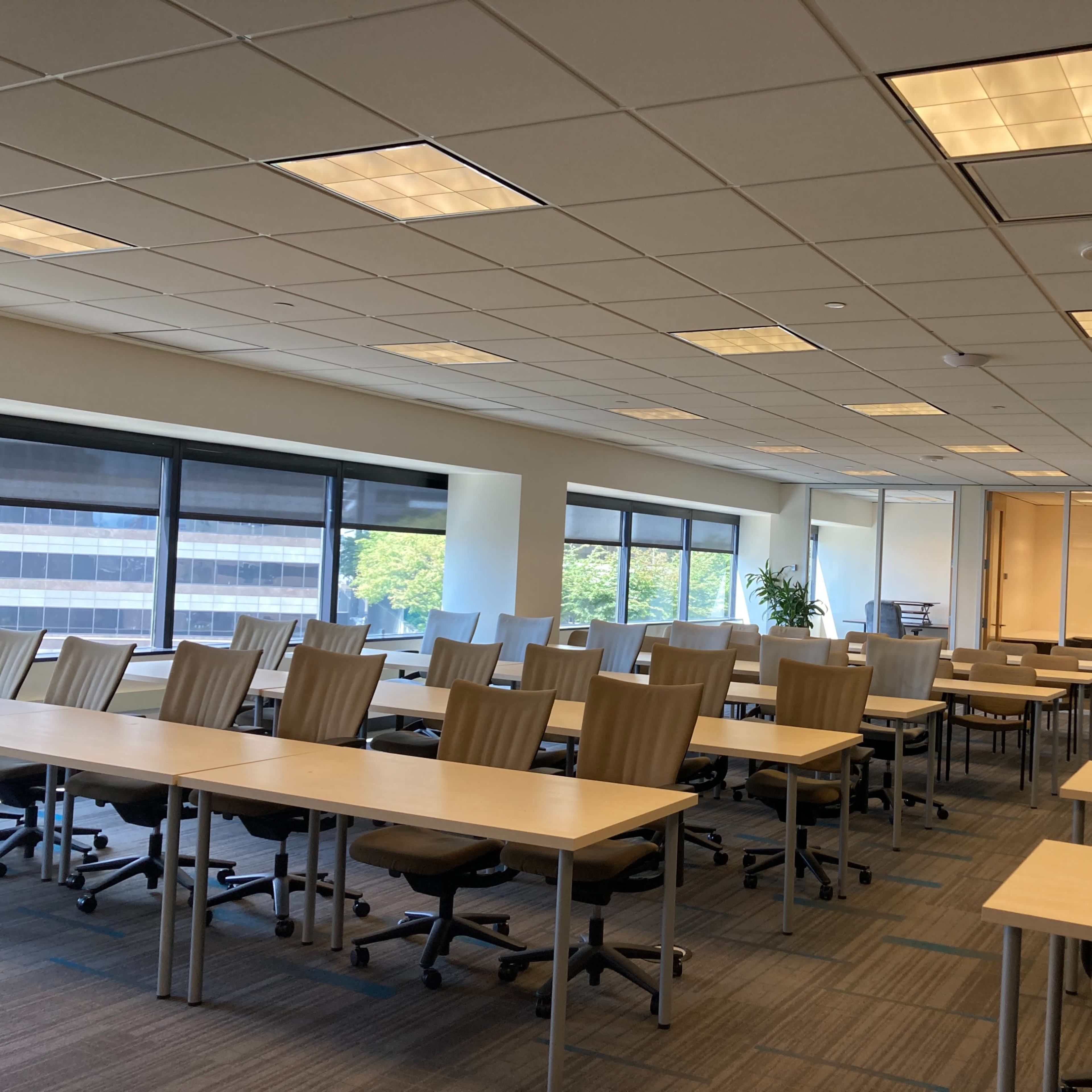 A spacious, modern classroom with multiple rows of desks and chairs, large windows, and a whiteboard.