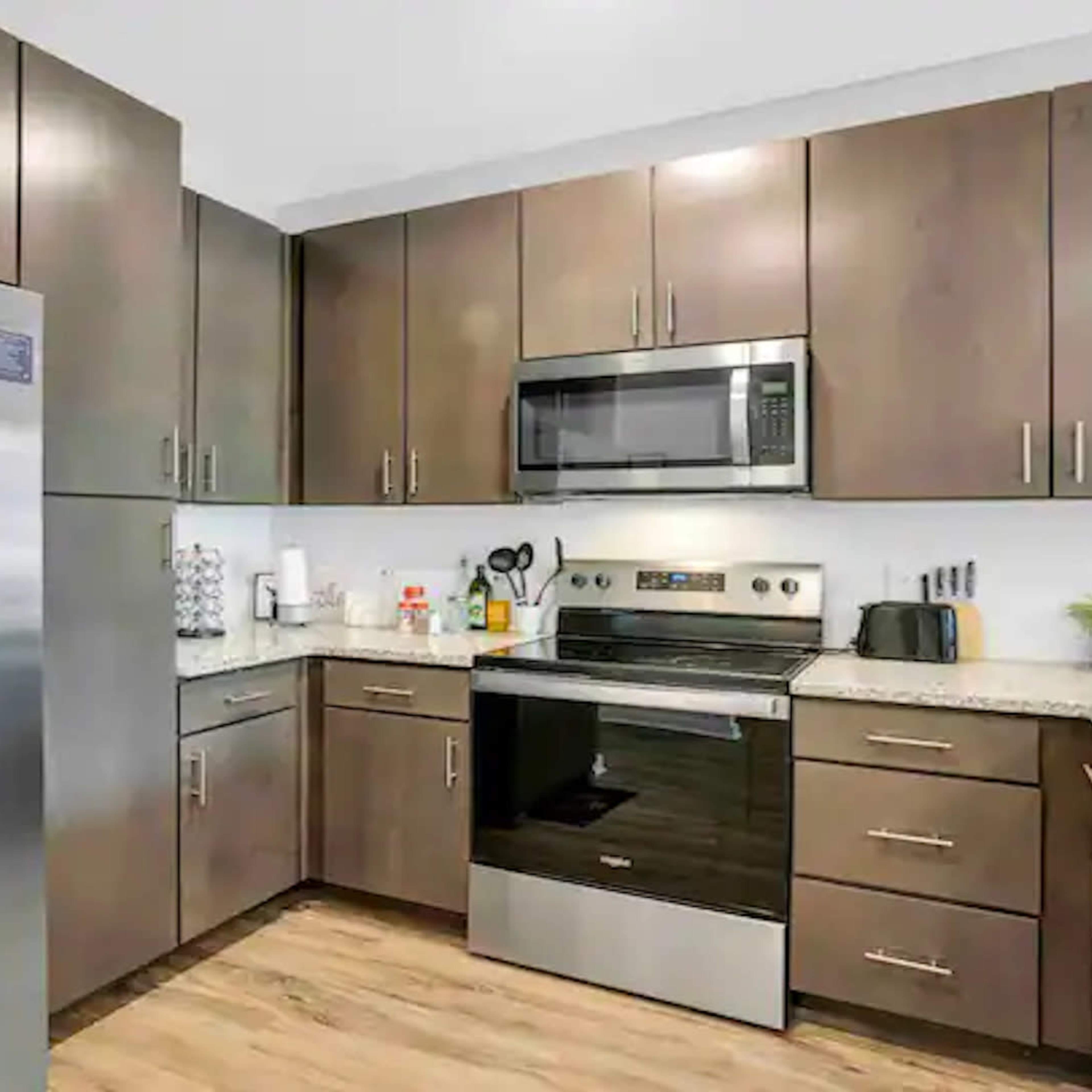 A modern kitchen with stainless steel appliances, including a refrigerator and microwave, and wooden cabinetry.