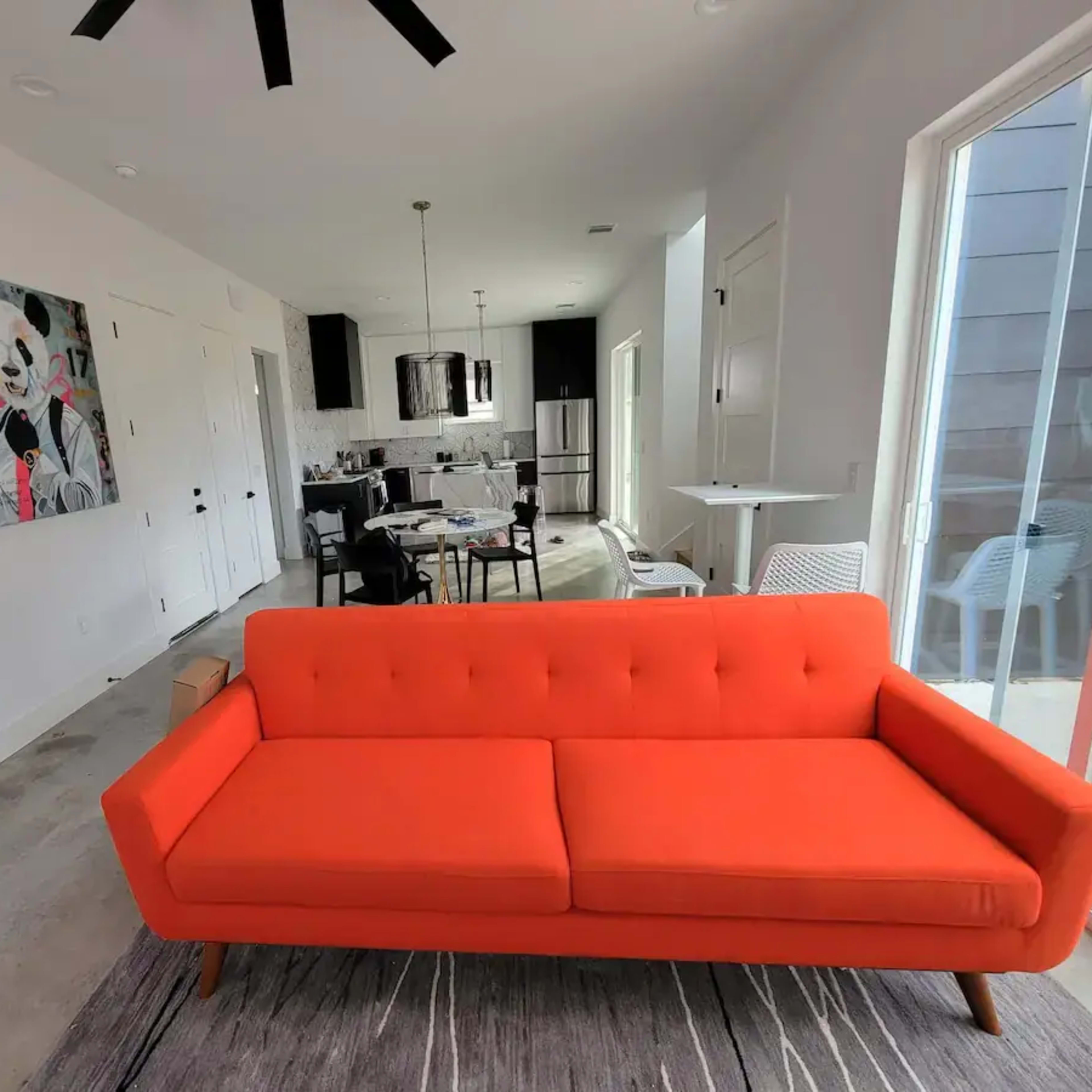 An orange sofa in a contemporary living space, with a dining area and kitchen visible in the background.