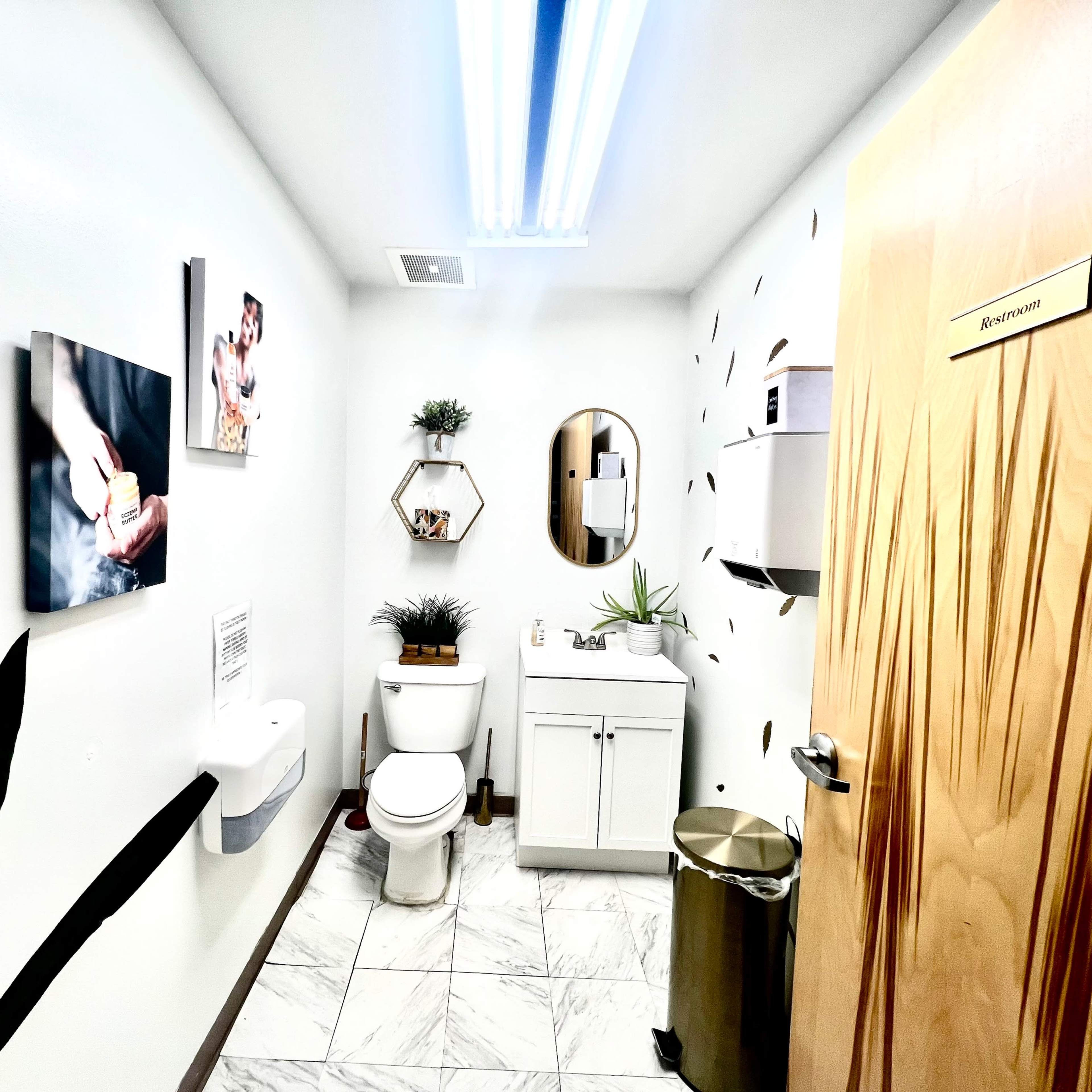 A clean bathroom with a toilet, a sink, a mirror, and decorative plants on the walls and counter.