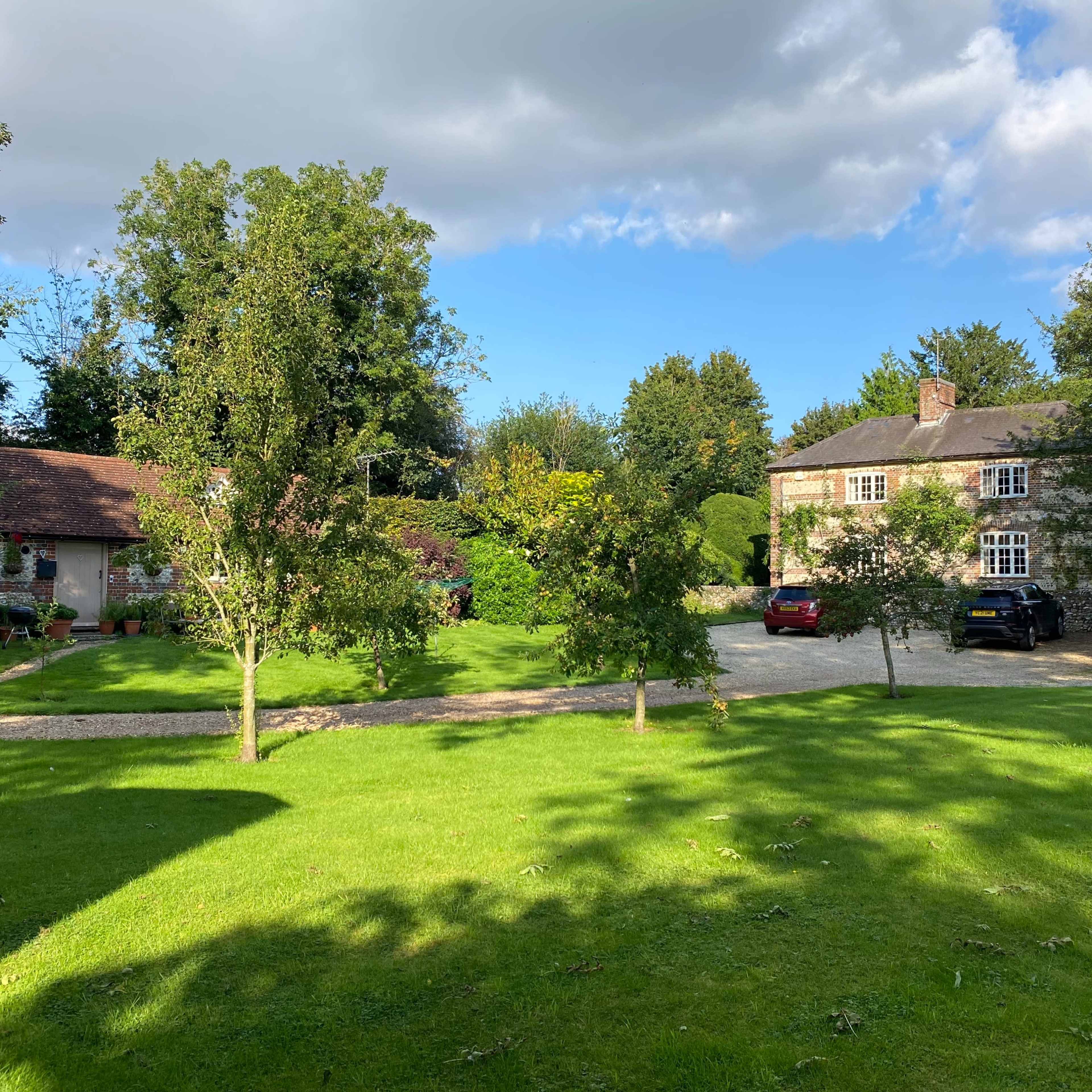 Two houses surrounded by a green lawn and trees under a partly cloudy sky.