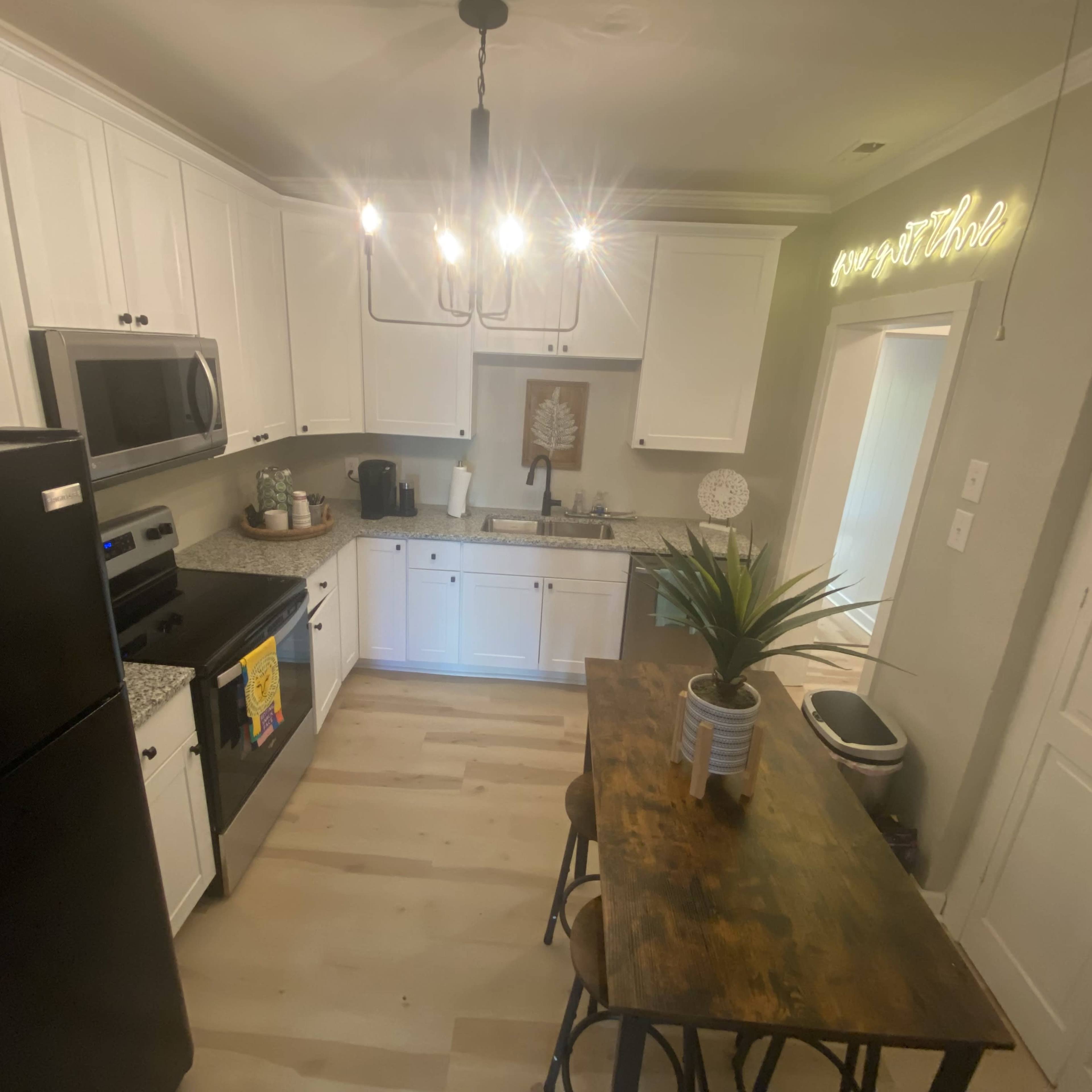 A modern kitchen features white cabinets, a black refrigerator, a wooden dining table with stools, and pendant lighting above.