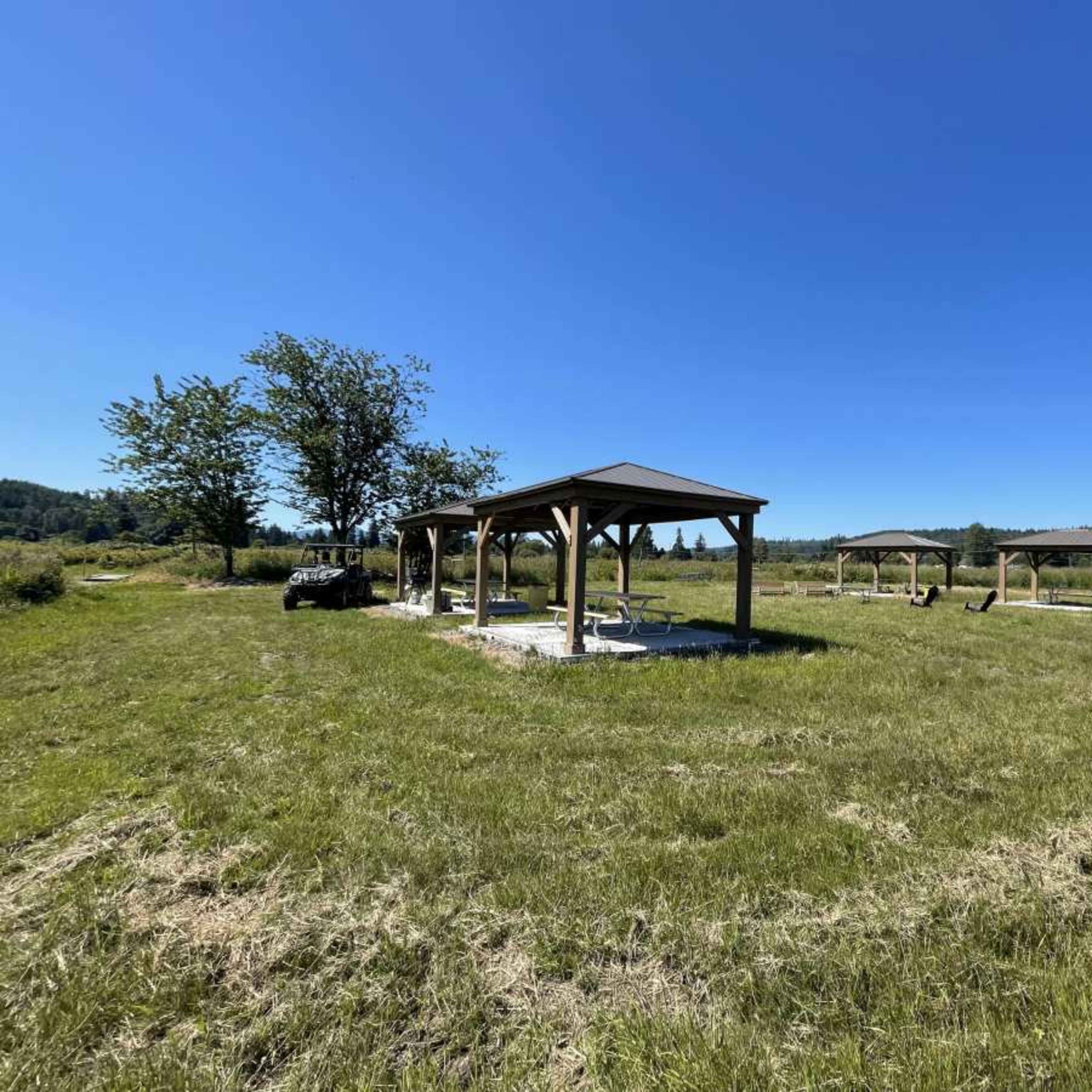 Several wooden pavilions situated in an open grassy field under a clear blue sky.