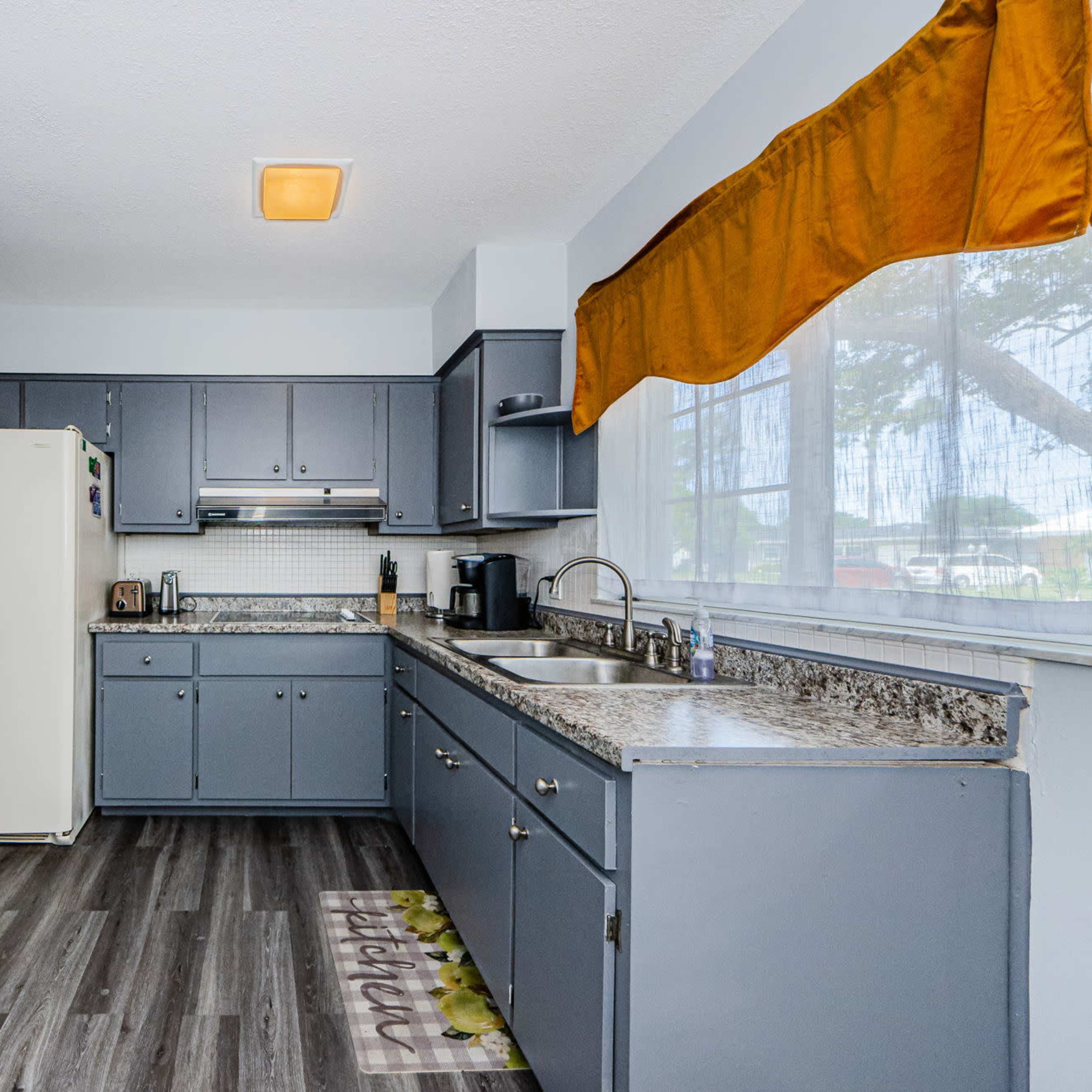 The kitchen features gray cabinetry, a granite countertop, and a window with an orange valance.