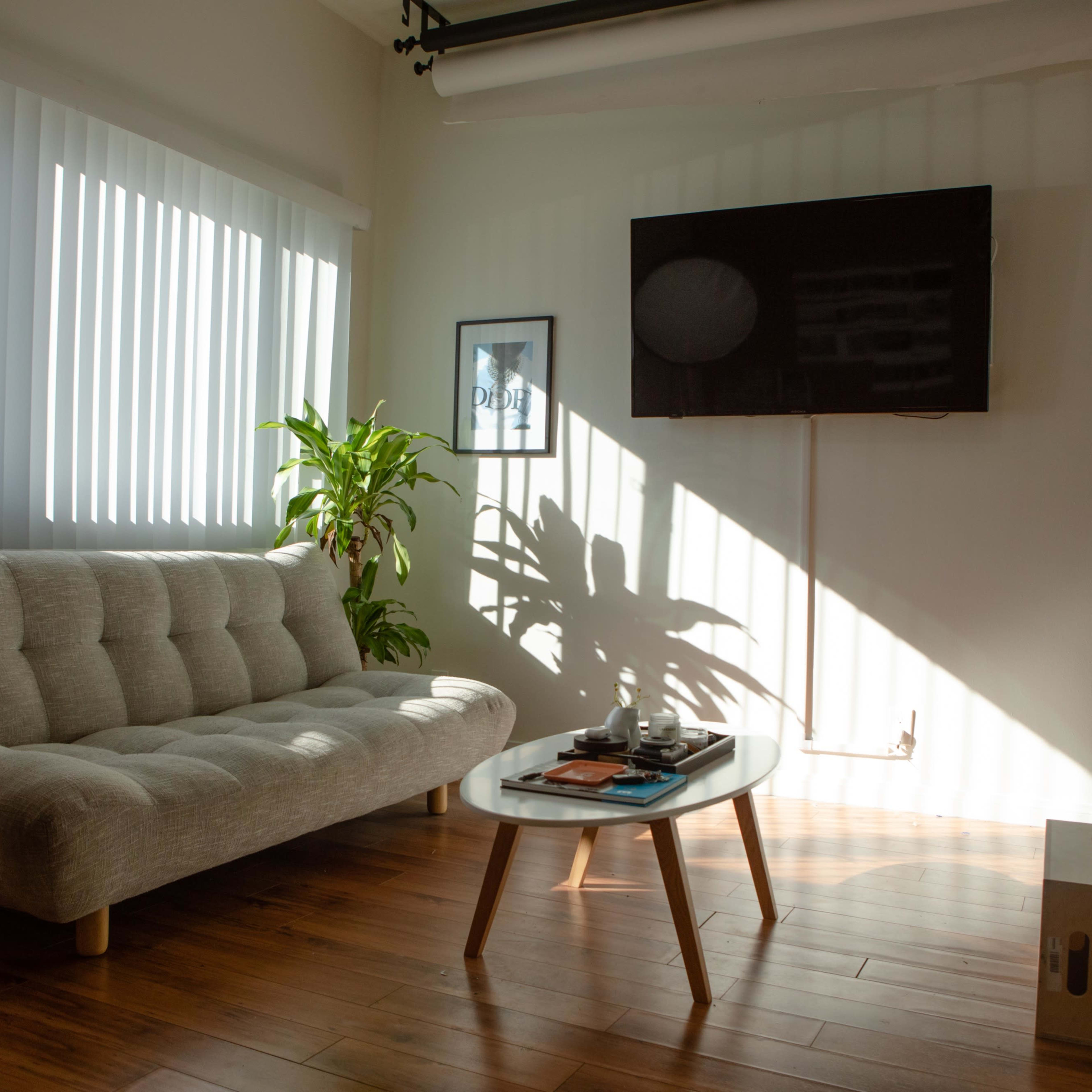 A light-filled living room features a gray sofa, a wooden coffee table with decor, and a television mounted on the wall.
