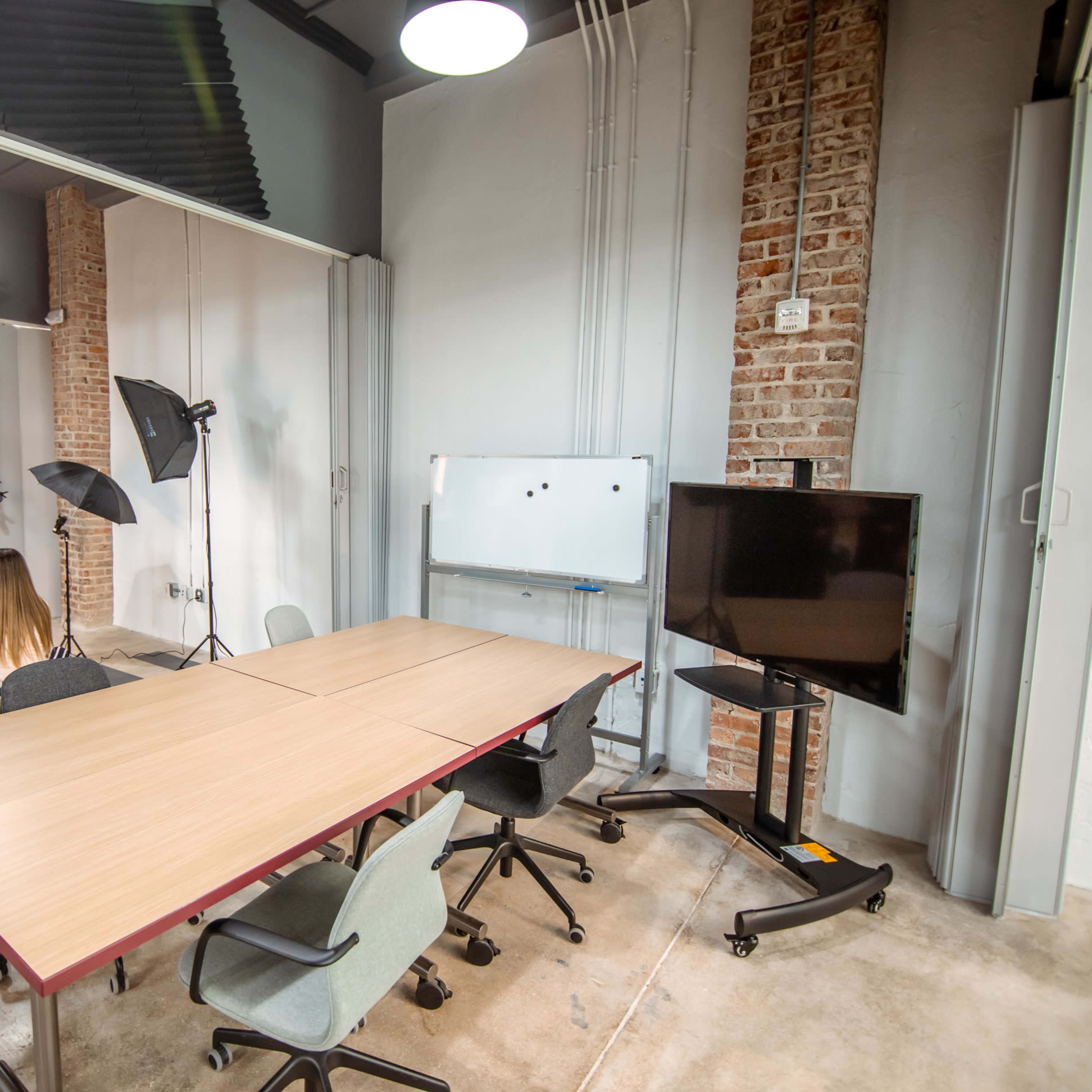 A photography studio features a black backdrop, a table with chairs, lighting equipment, and a television screen.