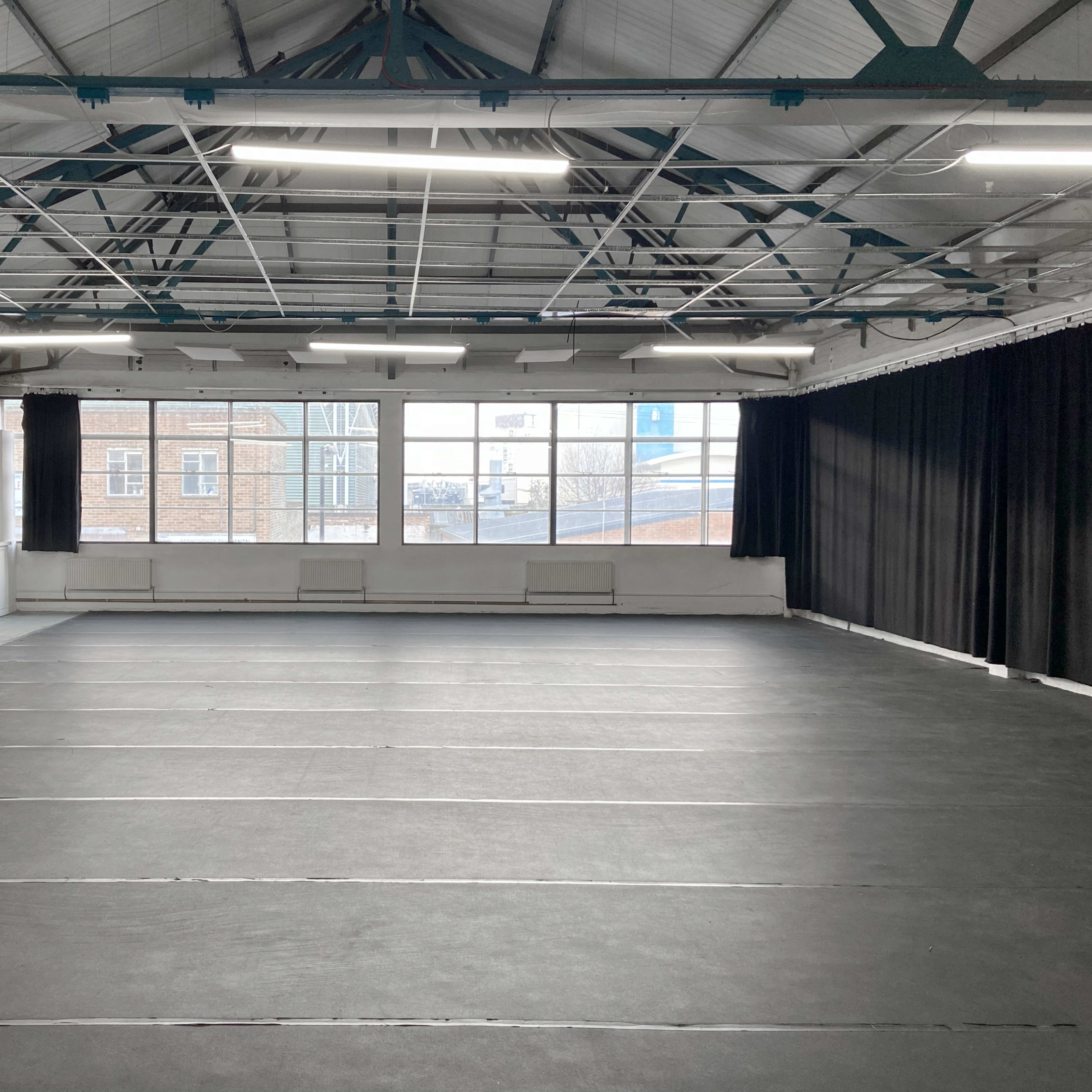A spacious, empty studio with a black mat floor and large windows letting in natural light.