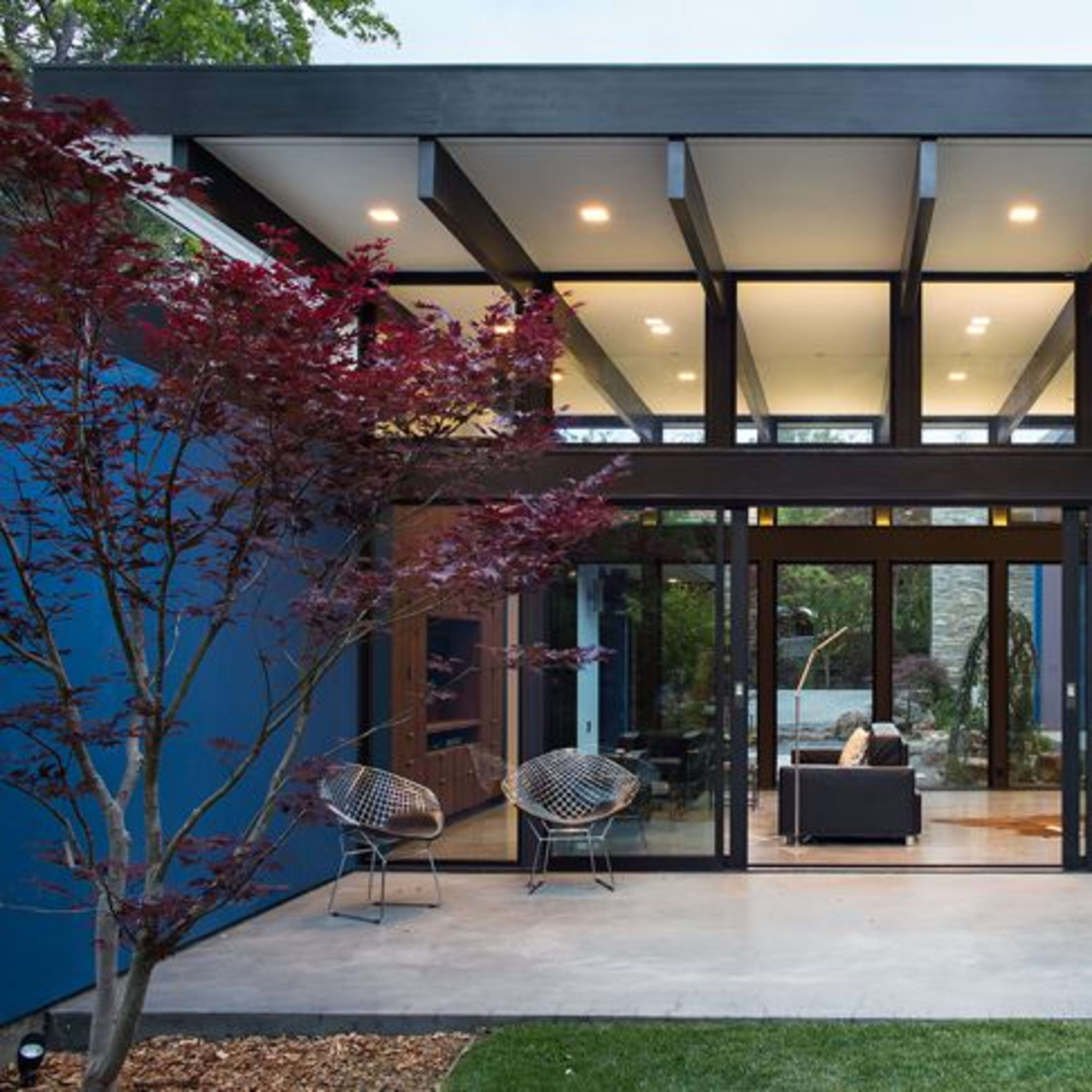 A modern house features large glass doors that open to a landscaped garden, with a sleek interior visible through the transparent walls.