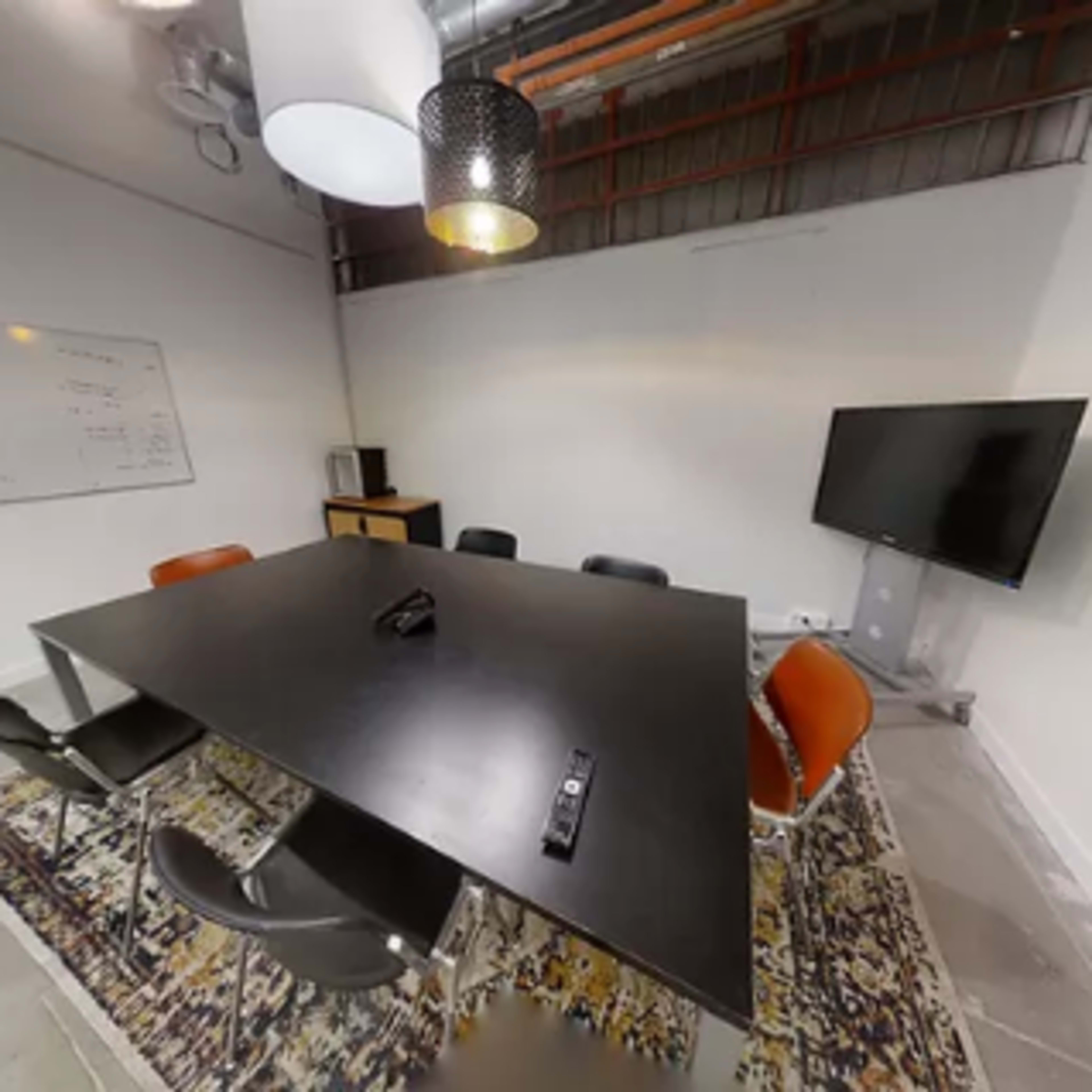 A modern conference room features a large black table surrounded by chairs, a television, and a whiteboard.
