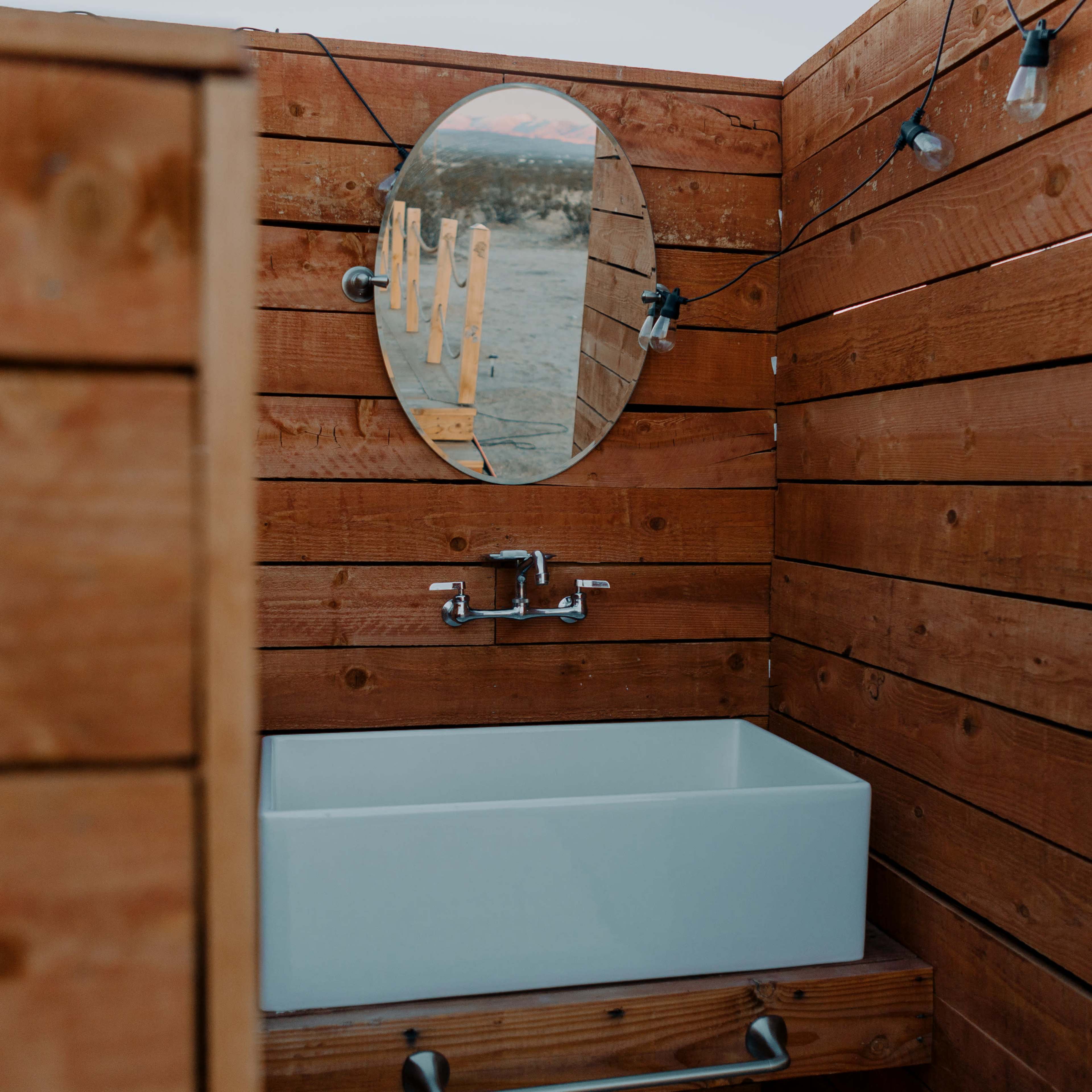 A wooden bathroom with a round mirror above a white sink, surrounded by wooden walls and soft lighting.