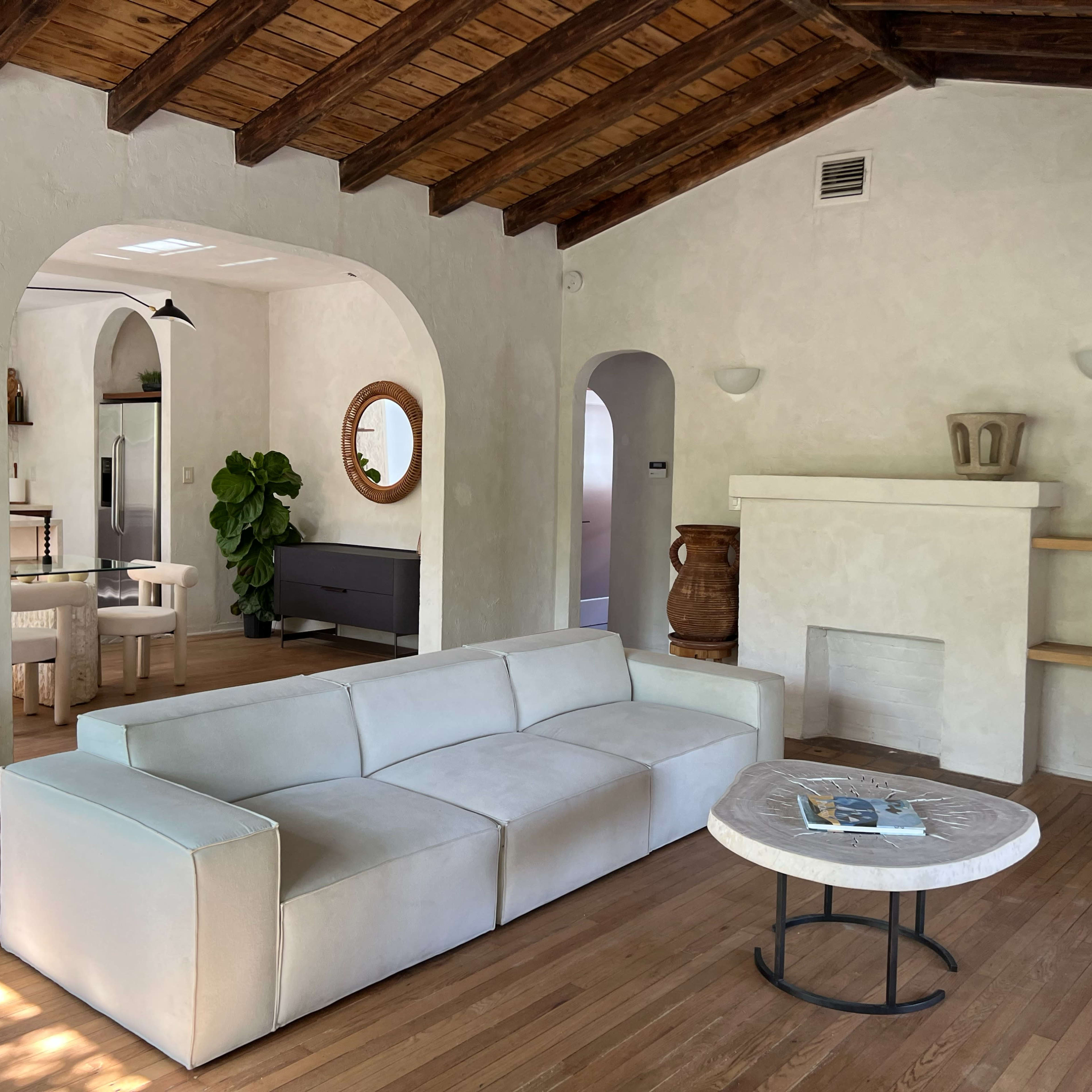A modern living room with a white sofa, wooden beams on the ceiling, and a round coffee table.