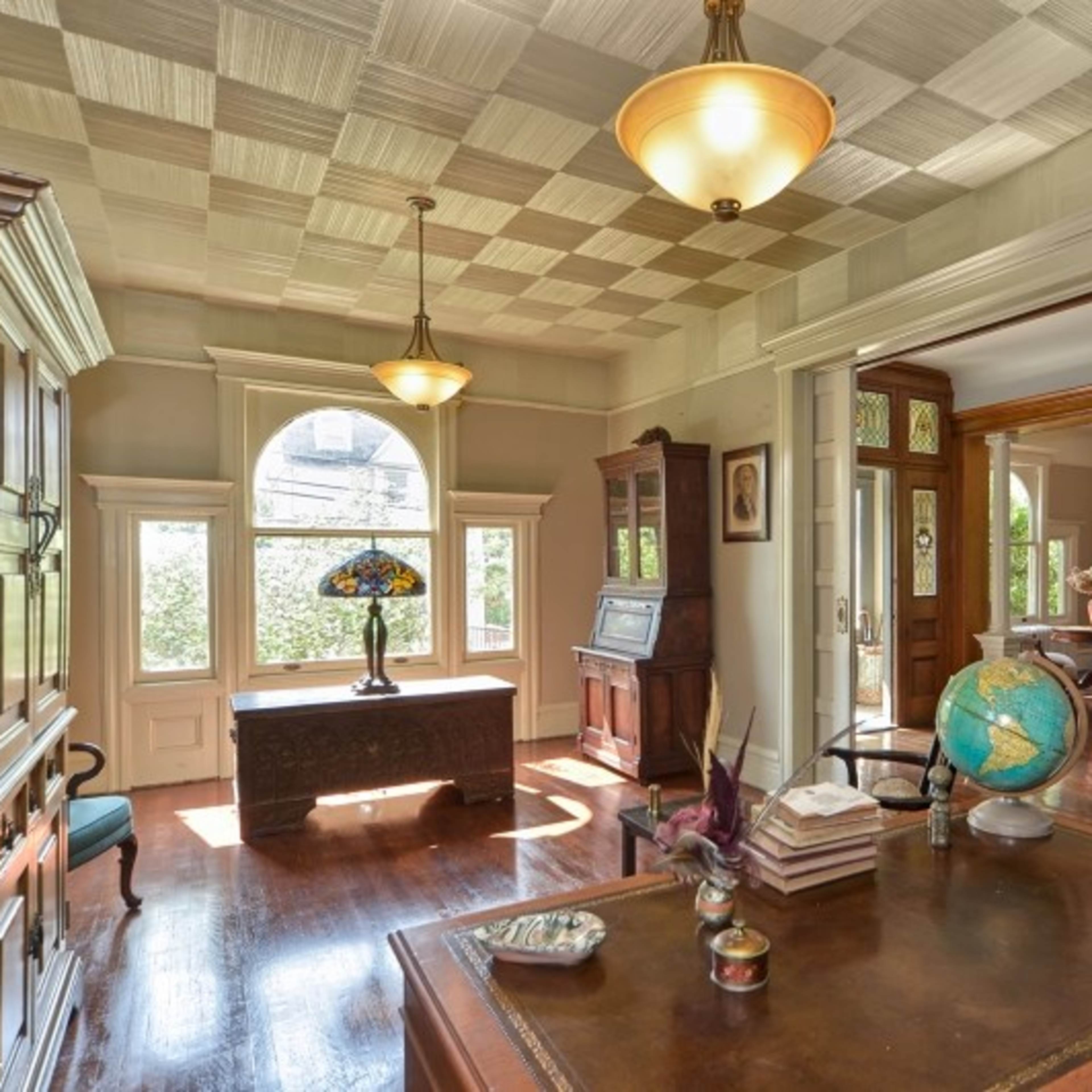 A well-lit room featuring a large window, antique furniture, and a globe on a wooden desk.