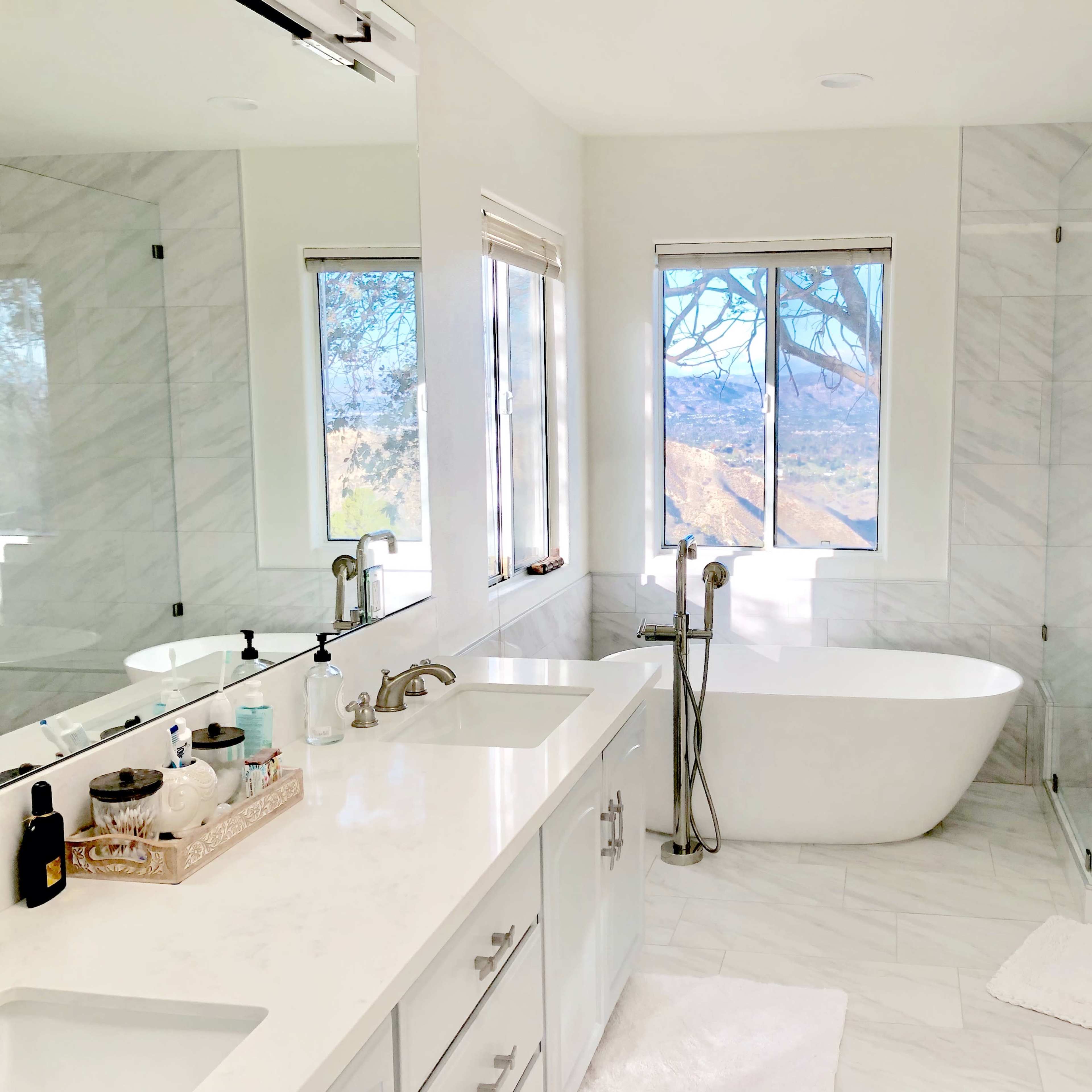 A modern bathroom featuring a freestanding bathtub, a glass shower, and a double vanity with a large mirror and natural light flowing in from a window.