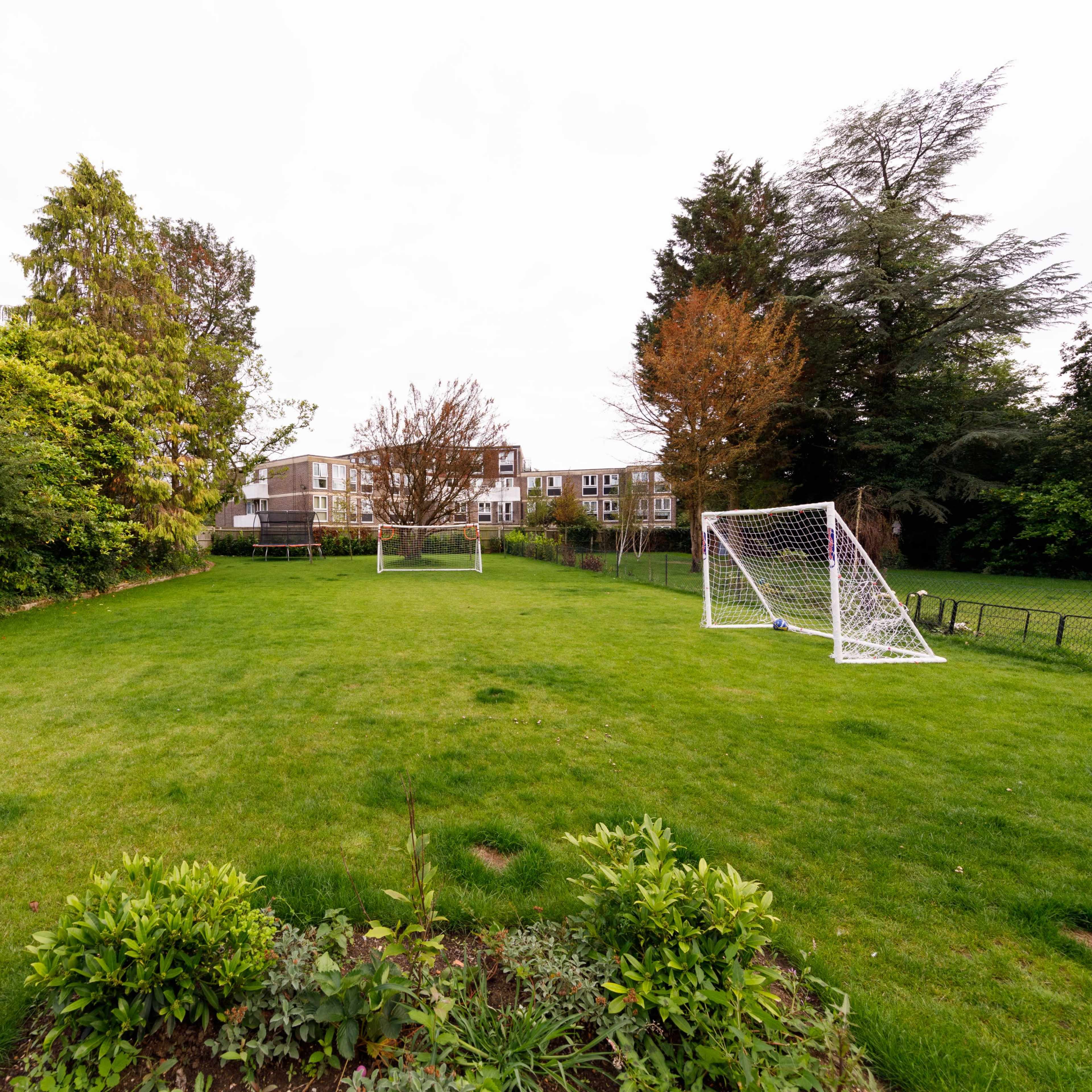 A grassy field with two soccer goals positioned at opposite ends and trees lining the background.