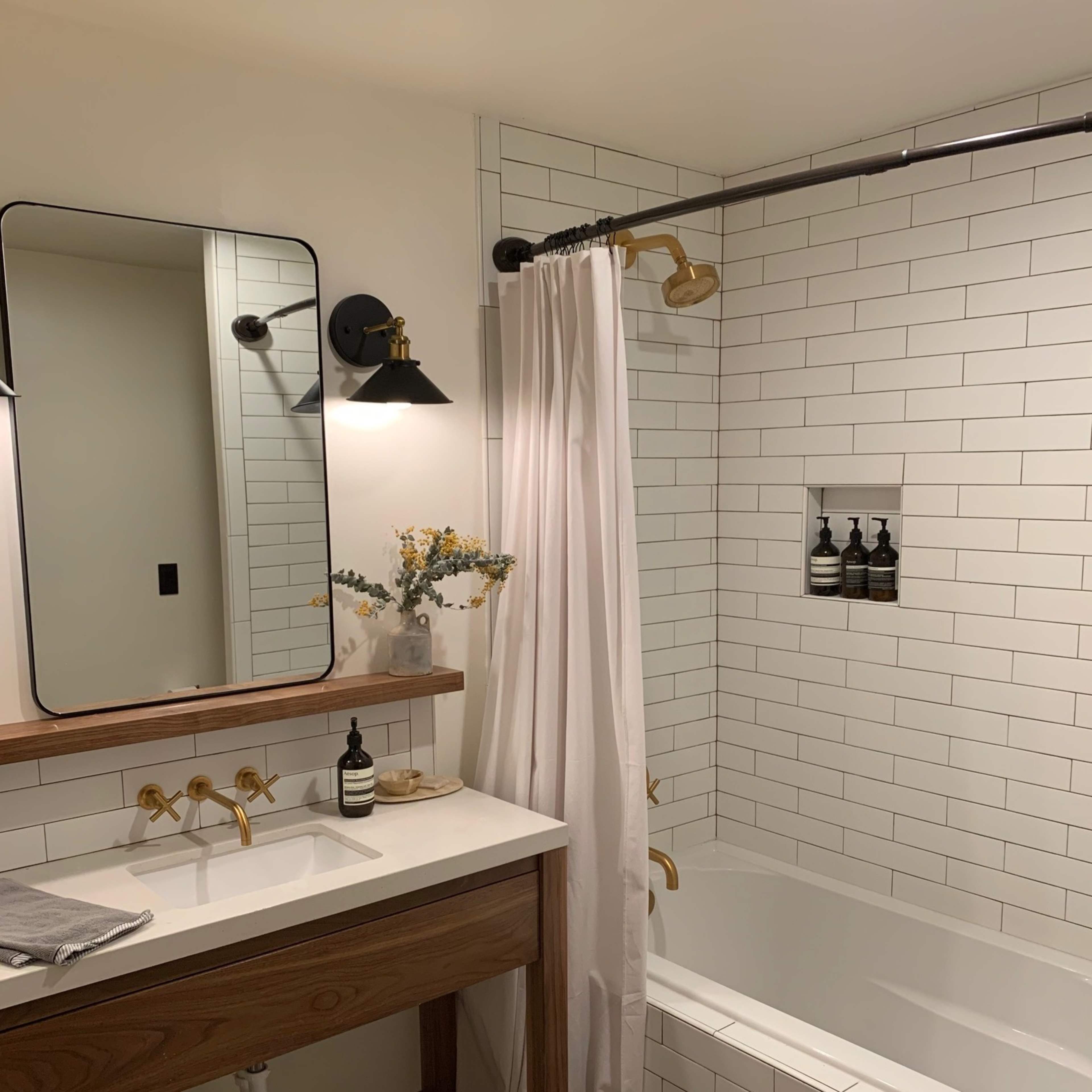 A modern bathroom with a wooden vanity, a large mirror, a bathtub surrounded by white tiles, and a shower curtain.