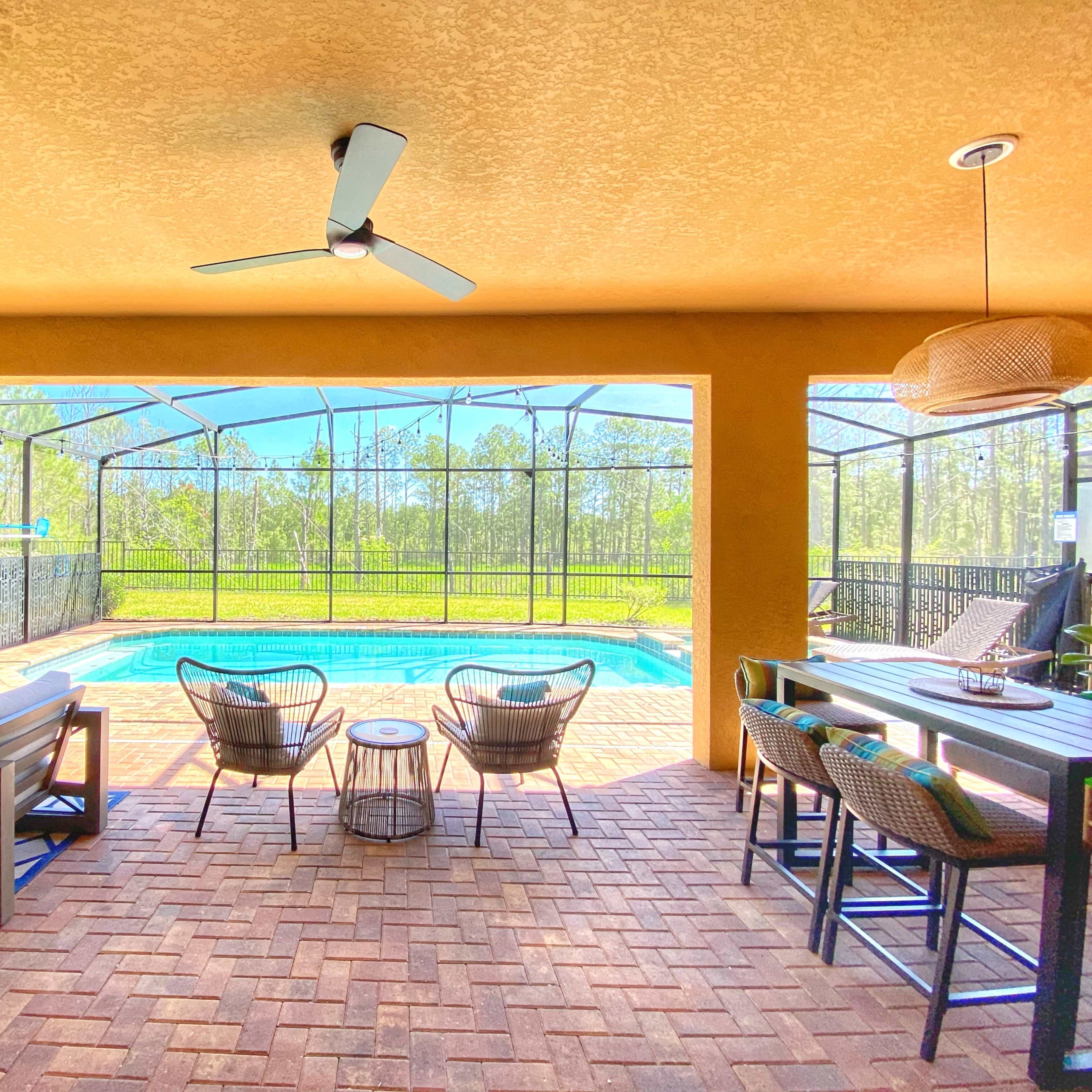 A covered patio area featuring a swimming pool, outdoor seating, and a dining space surrounded by a screened enclosure.