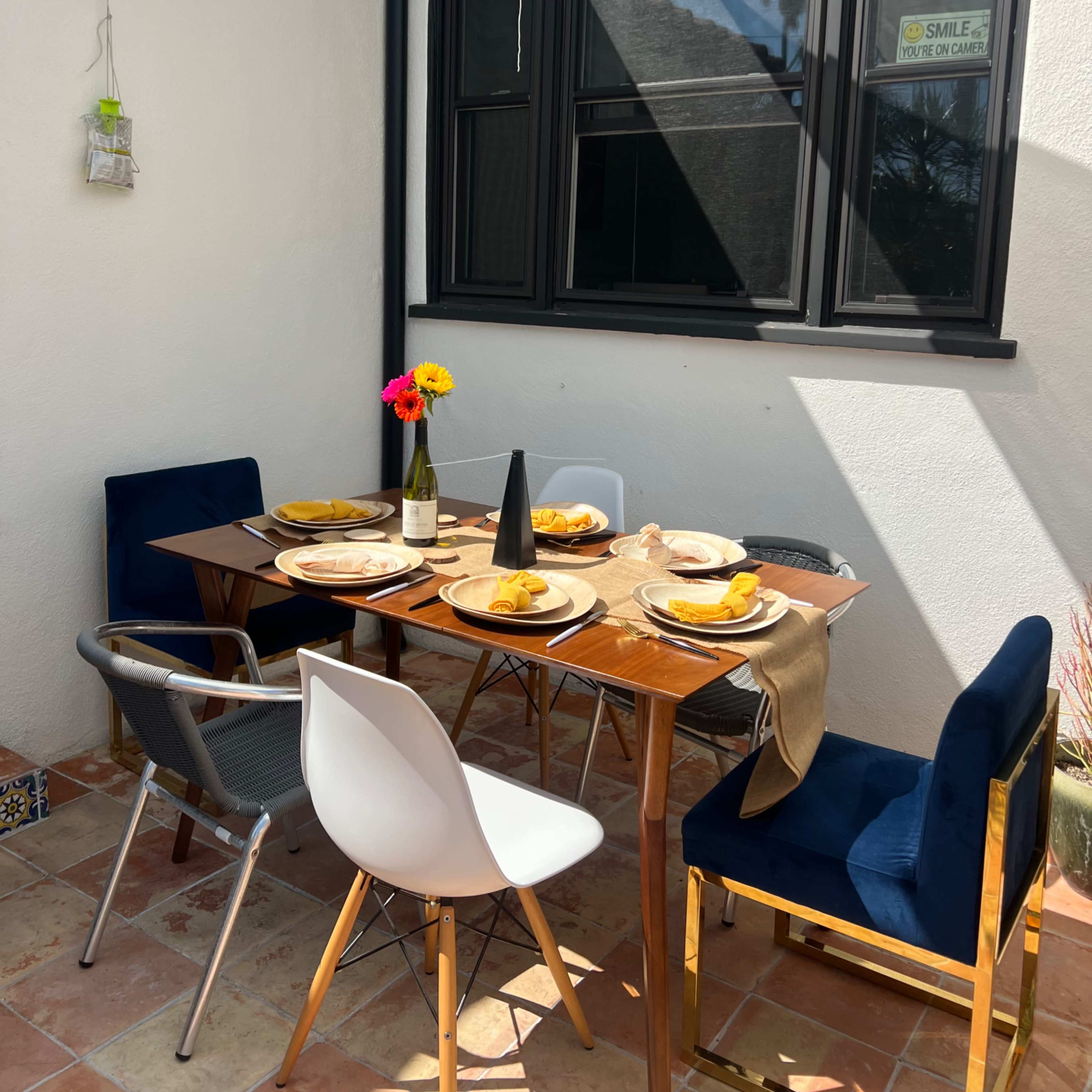 A wooden dining table is set with plates of food and flowers in a cozy outdoor patio space.