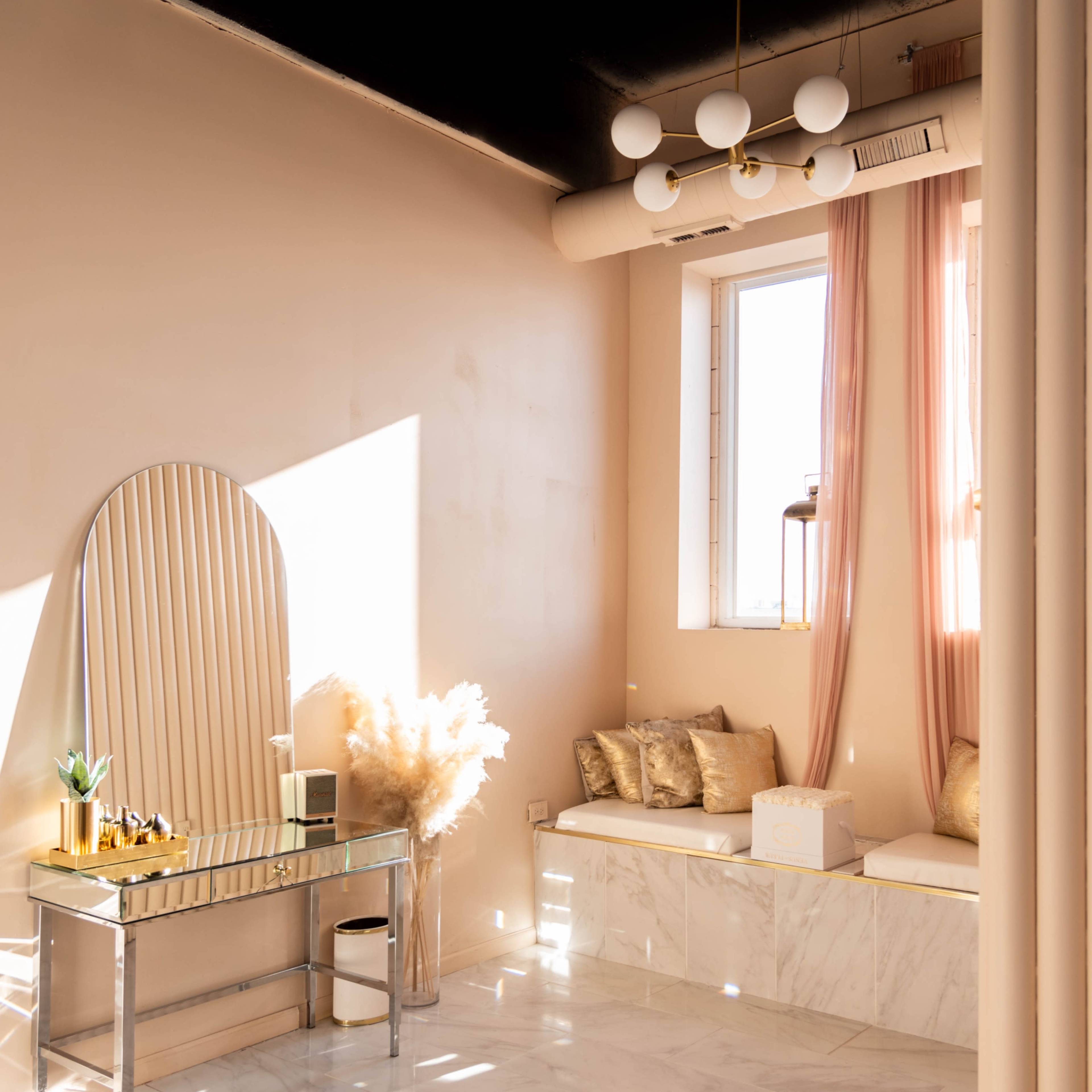 A minimalist interior space with a console table, plush seating, and decorative elements, illuminated by natural light streaming through a window.