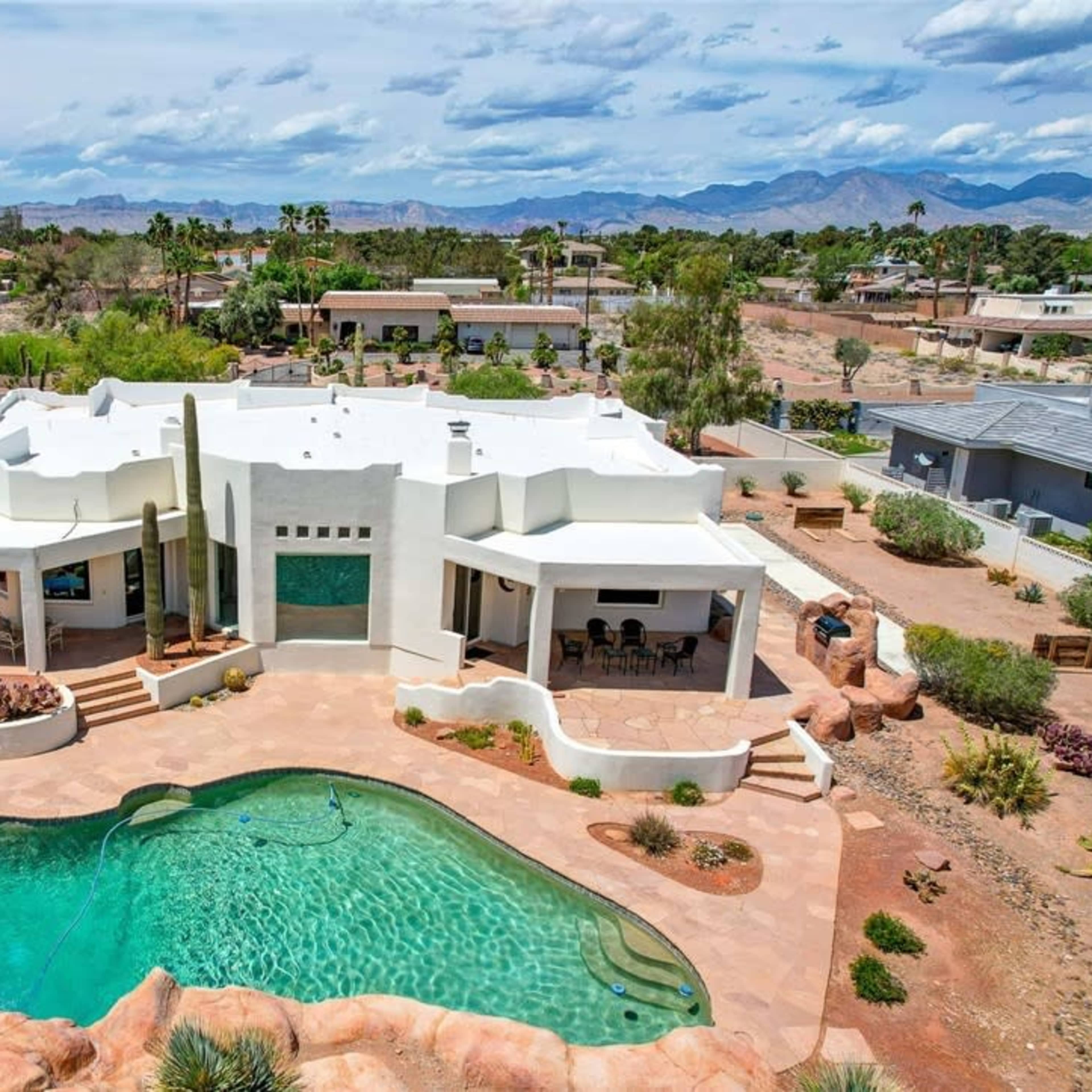 A modern white house with a pool surrounded by rocks and a desert landscape, with mountains in the background.