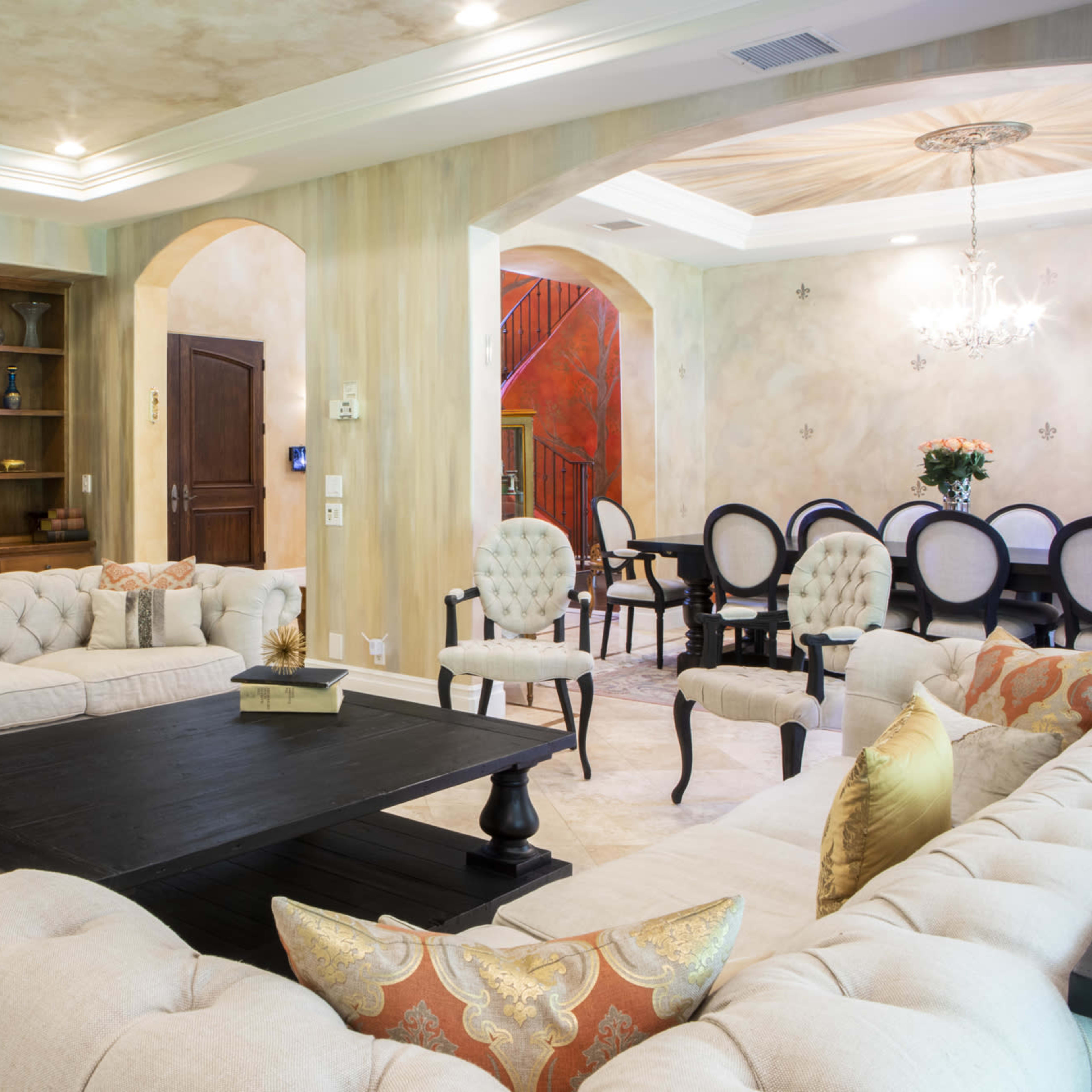A spacious, elegantly arranged living room with a central coffee table and plush sofas, transitioning to a dining area with a large table and decorative chandelier.