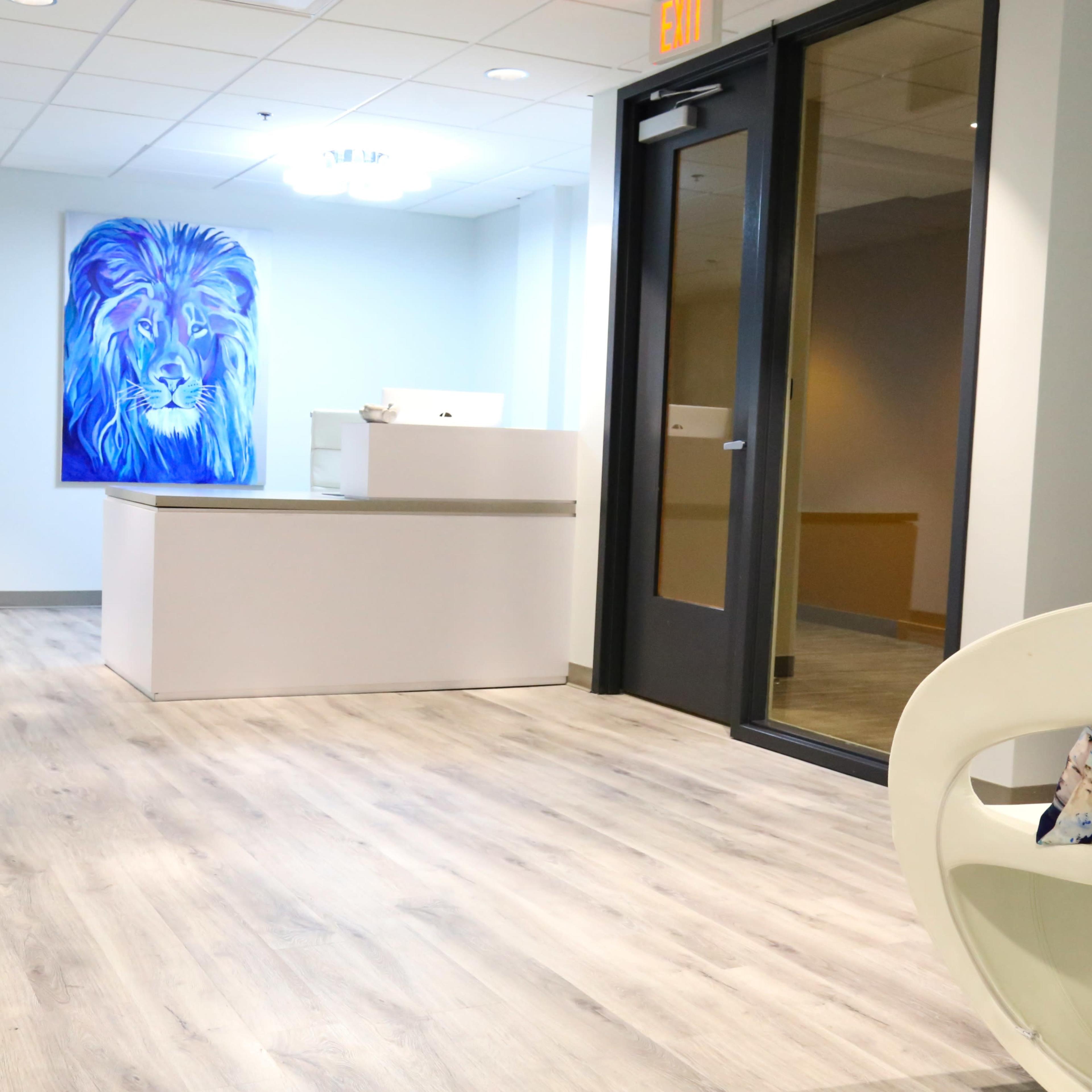 A modern hallway with a reception desk at the end, featuring a large lion painting on the wall and minimalist furniture.