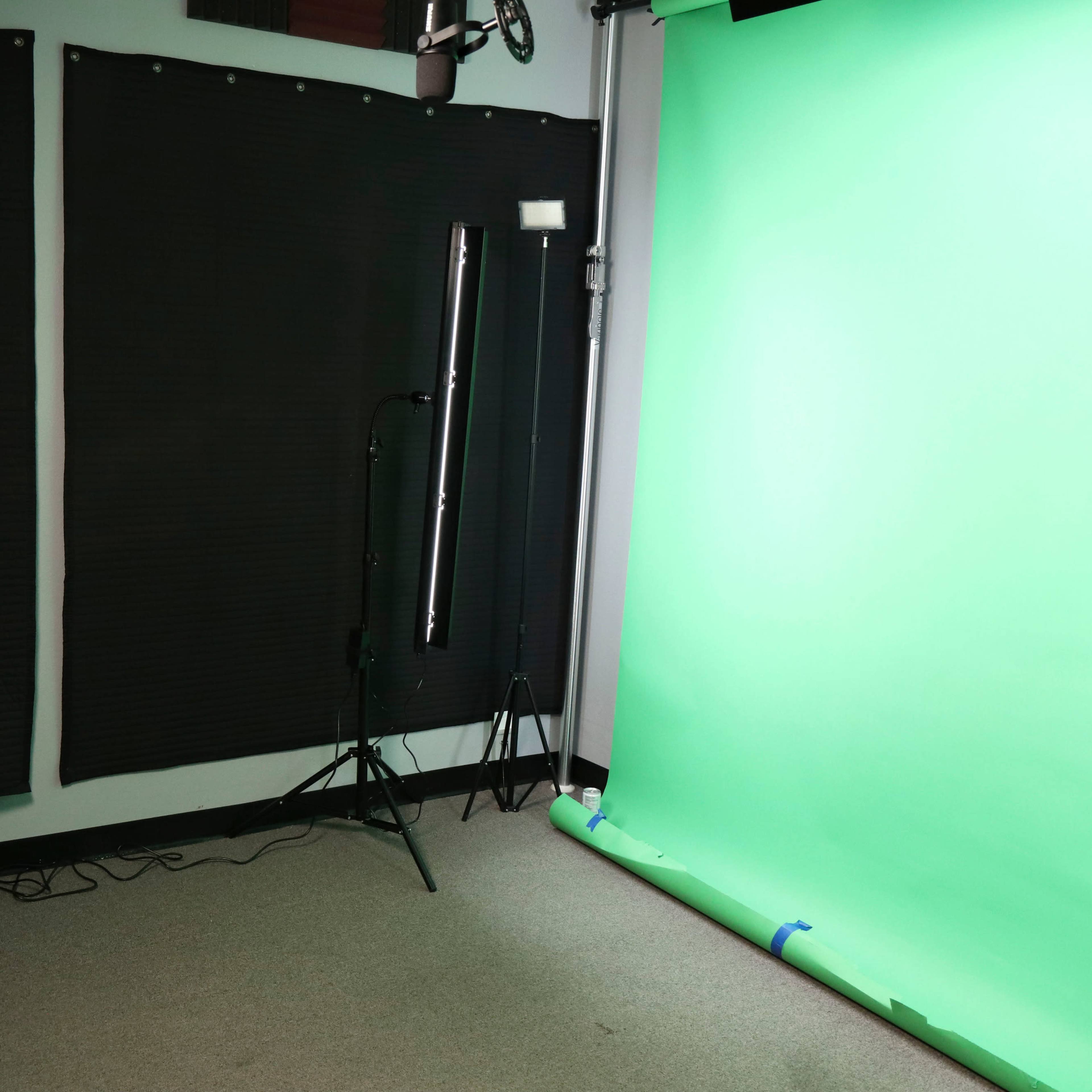 A video production studio with a green chroma key backdrop, a computer setup, and lighting equipment.