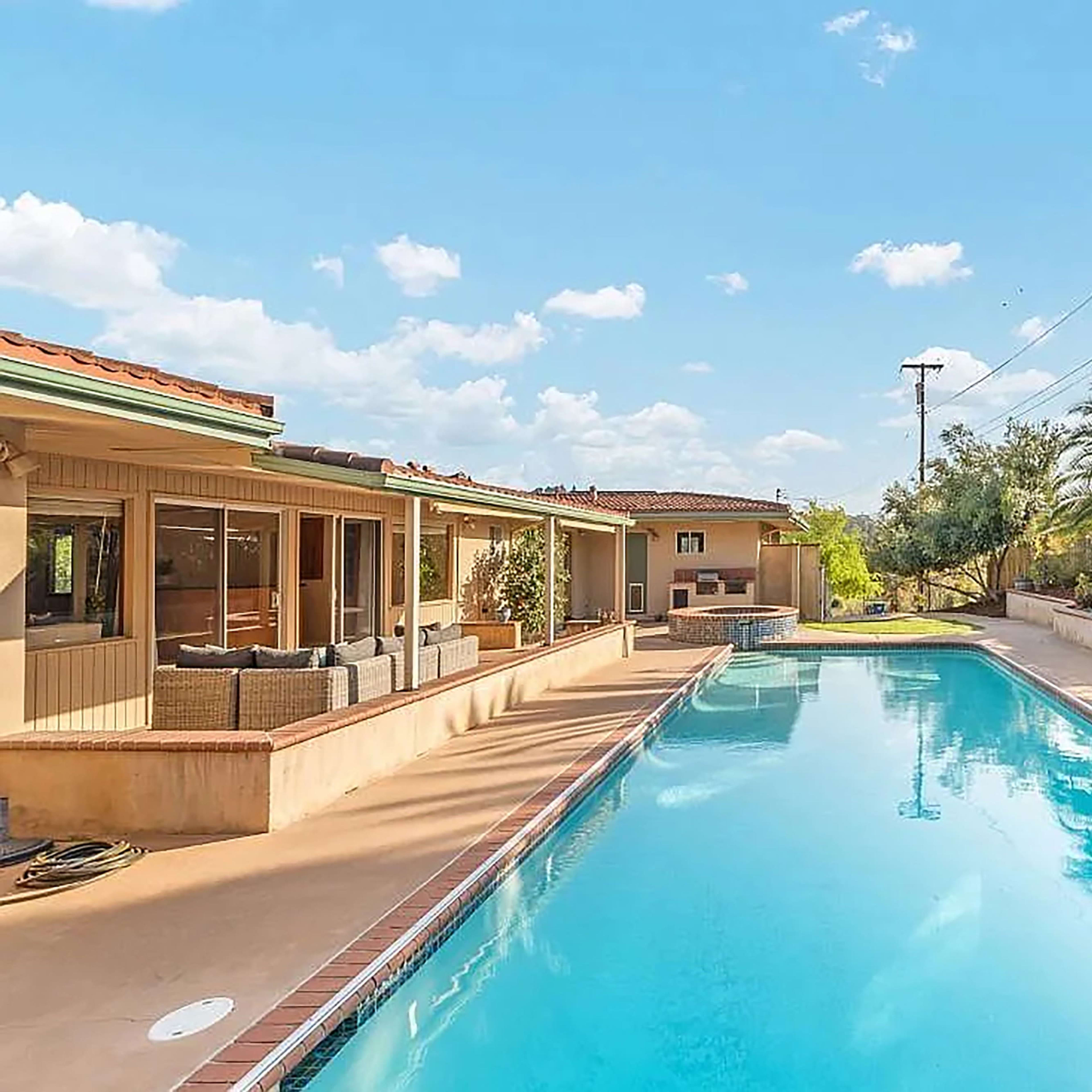A clear swimming pool surrounded by a landscaped garden and a residential building under a blue sky.