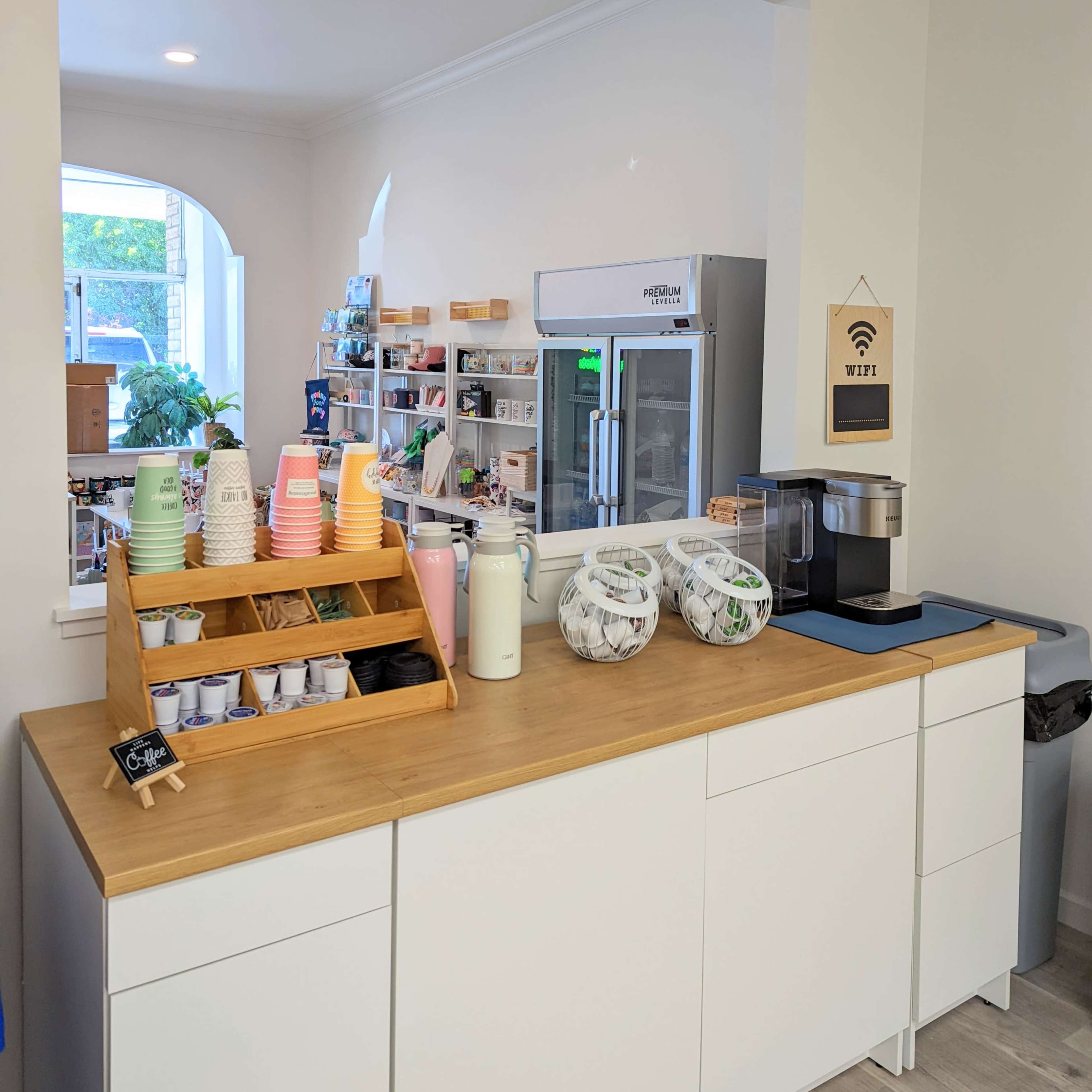 A service counter features a variety of cups and condiments, a beverage dispenser, and a refrigerator in a bright, open space.