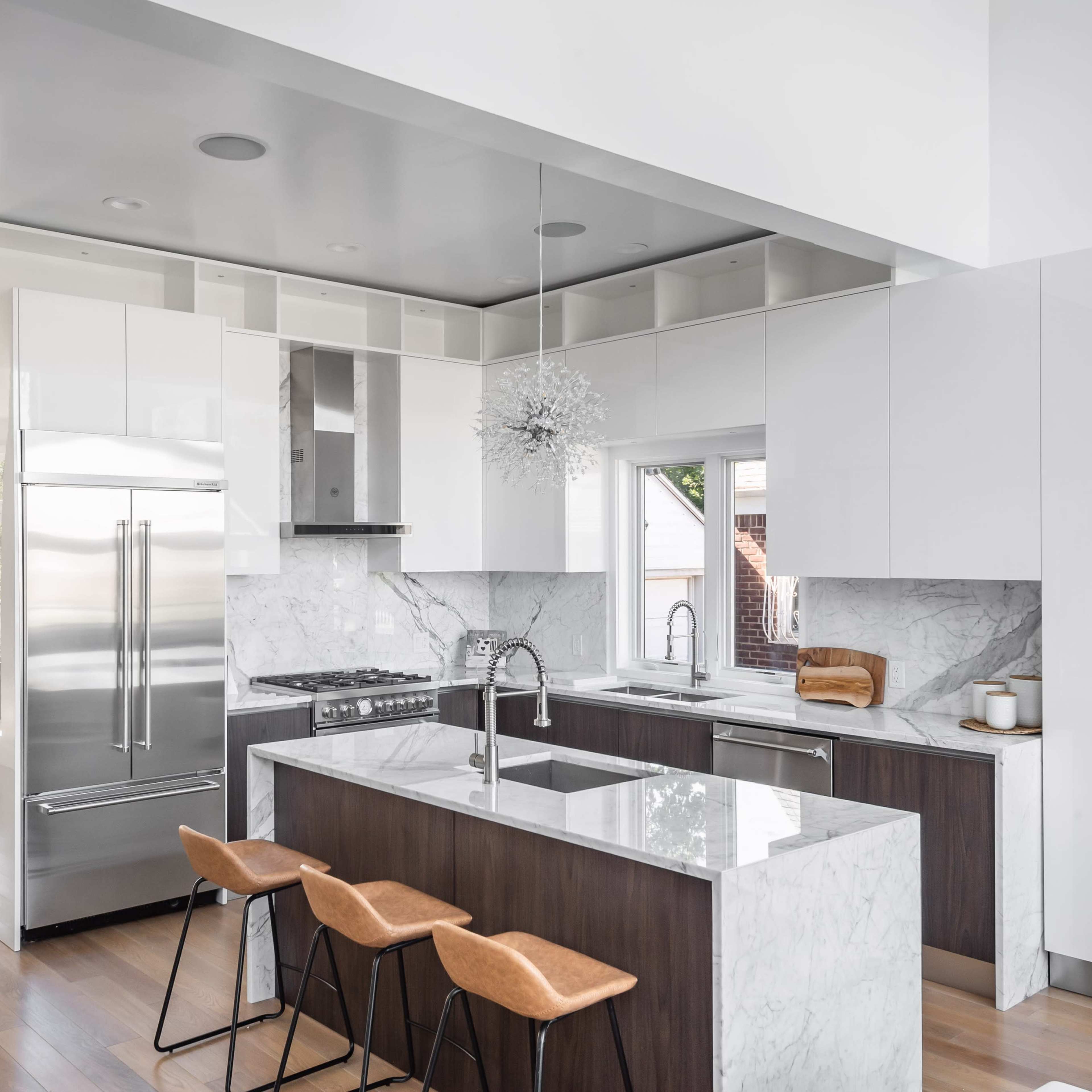 A modern kitchen featuring a marble island, stainless steel appliances, and wooden bar stools.