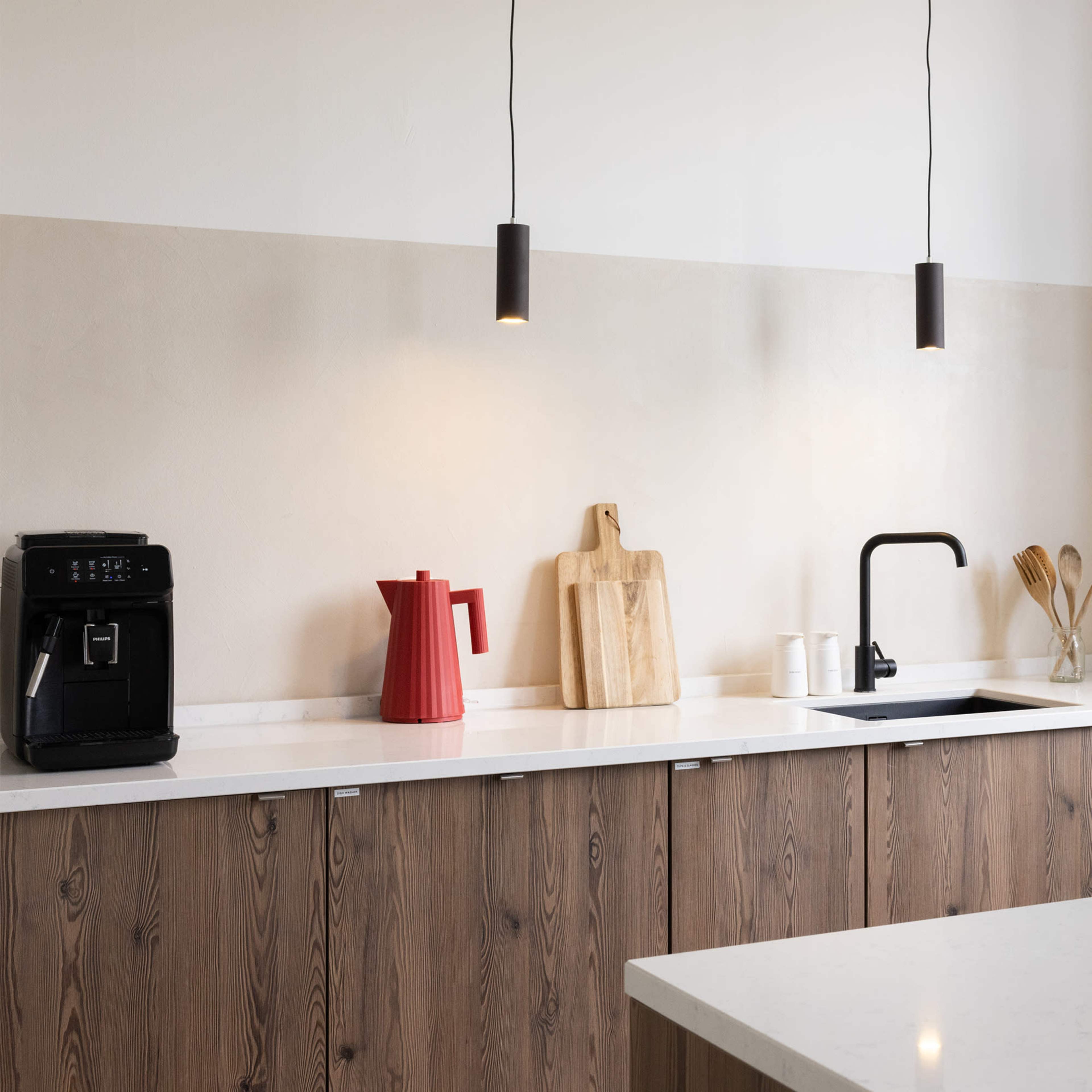 A modern kitchen features wooden cabinetry, a white countertop, a black sink, and pendant lighting above the workspace.