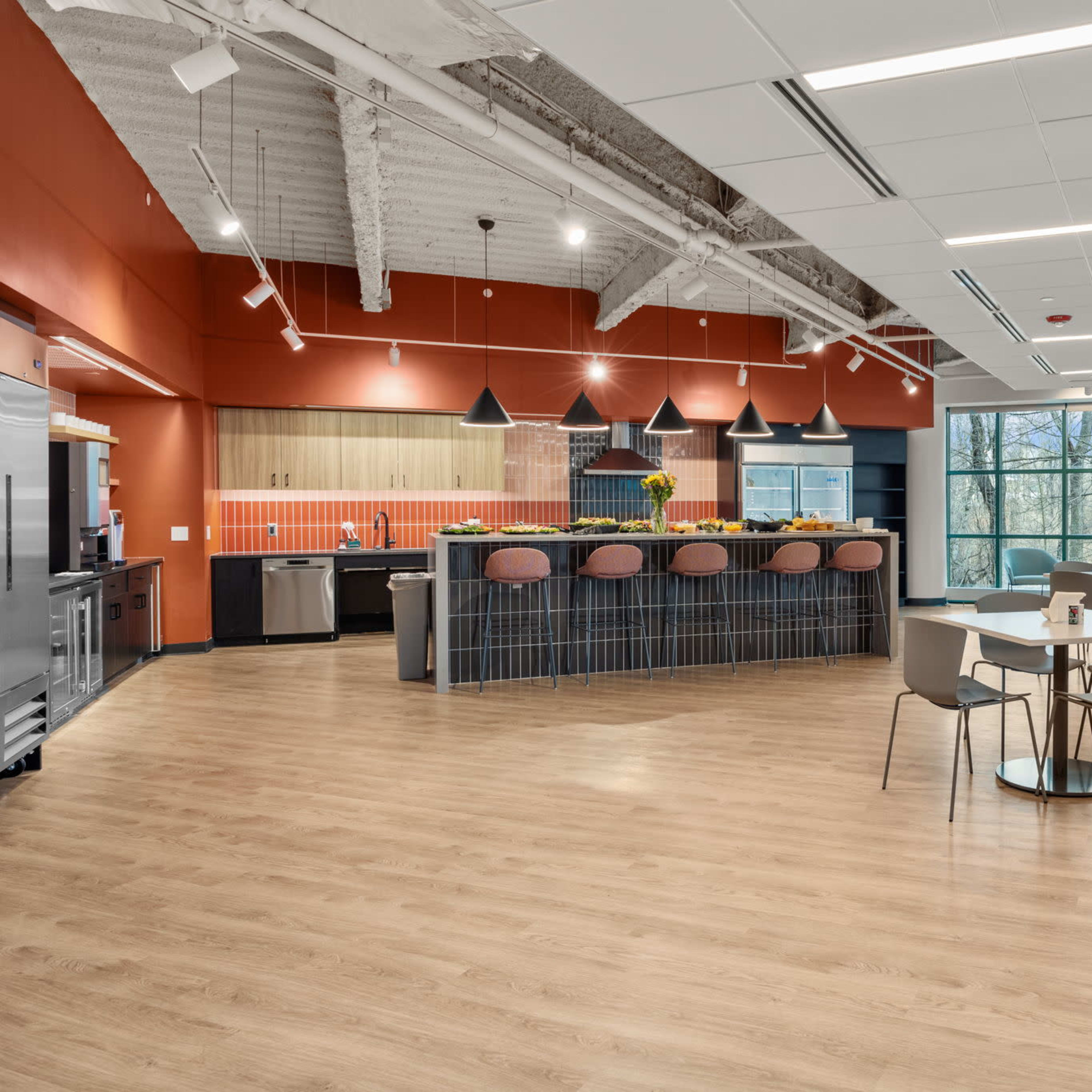 A modern kitchen and dining area with a large window overlooking a natural landscape, featuring a central island with bar seating and various kitchen appliances.