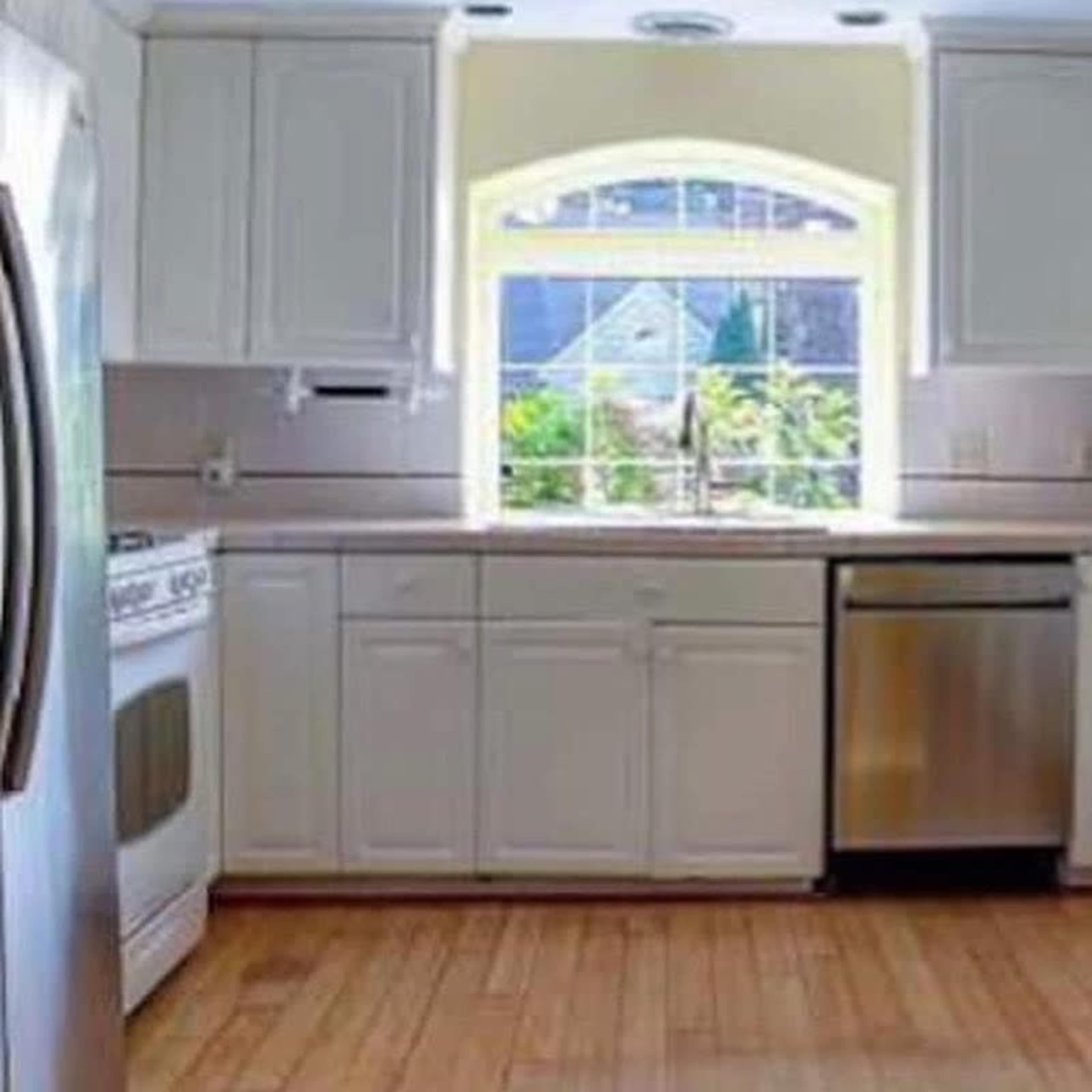 A modern kitchen with white cabinets, stainless steel appliances, and a window overlooking a garden.