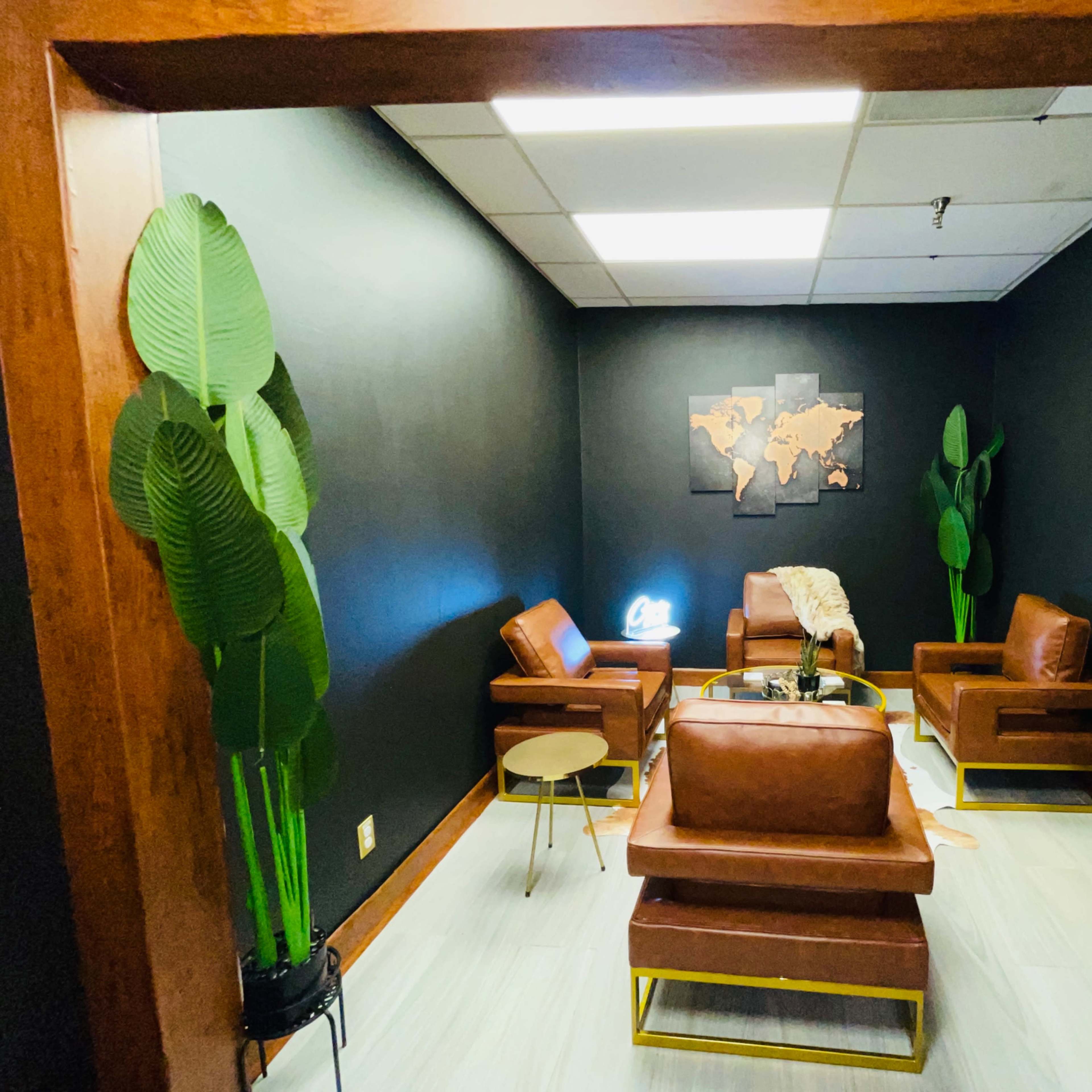 A modern lounge area with brown leather chairs, a small circular table, and potted plants, all set against a black wall featuring a world map.