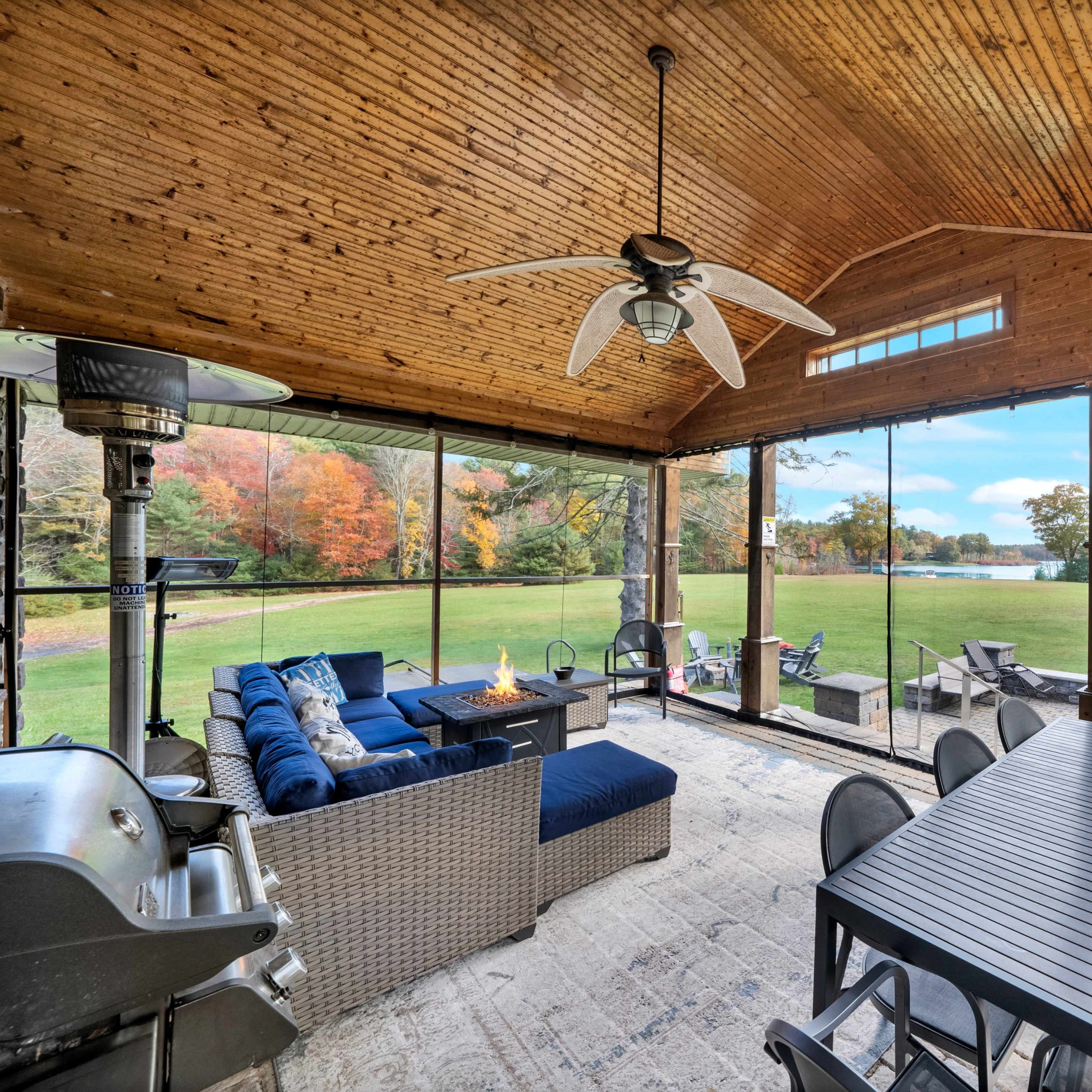 A screened porch with a dining table and seating area overlooking a green yard surrounded by trees.