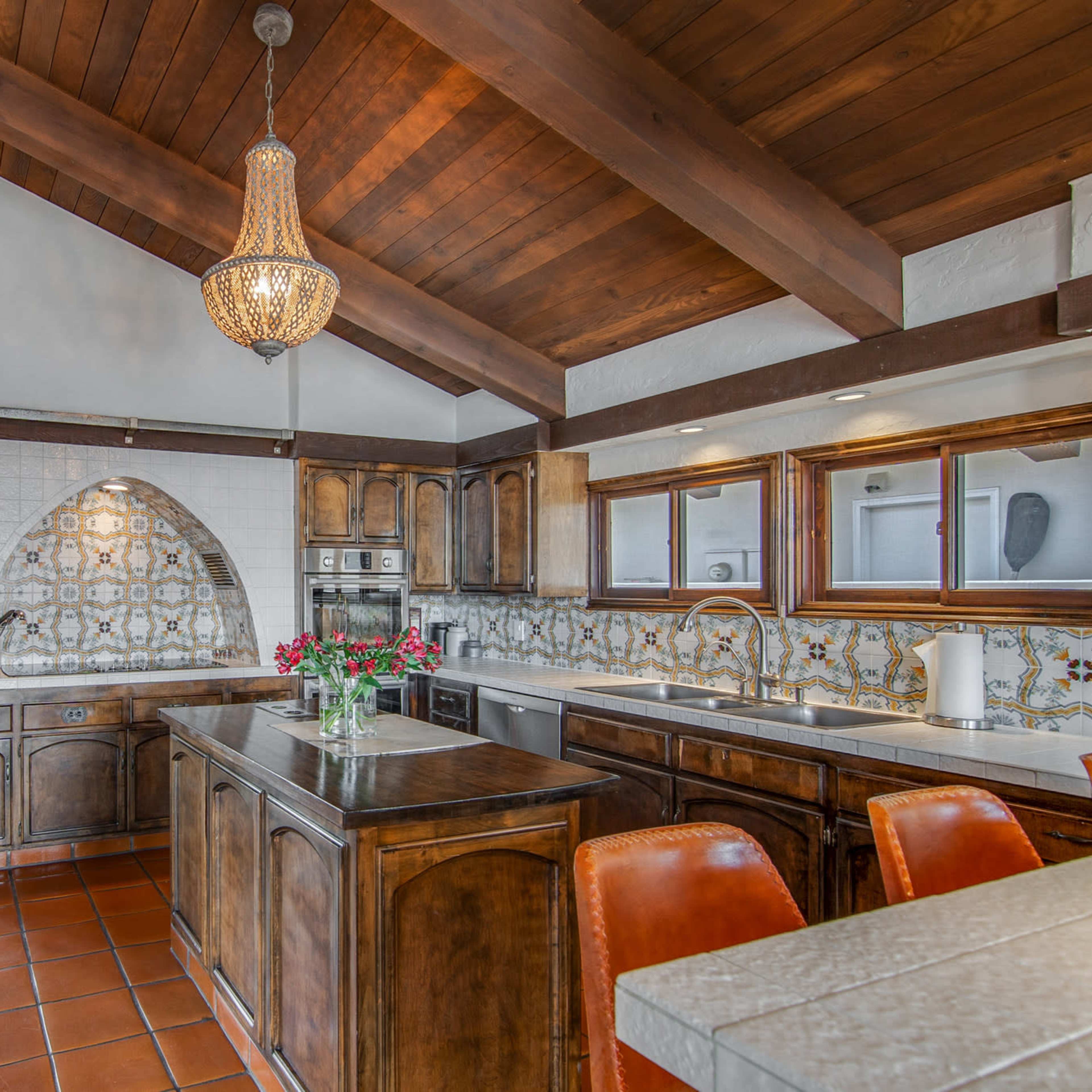 A spacious kitchen features wooden cabinetry, a tile backsplash with decorative patterns, and a large central island with bar seating.
