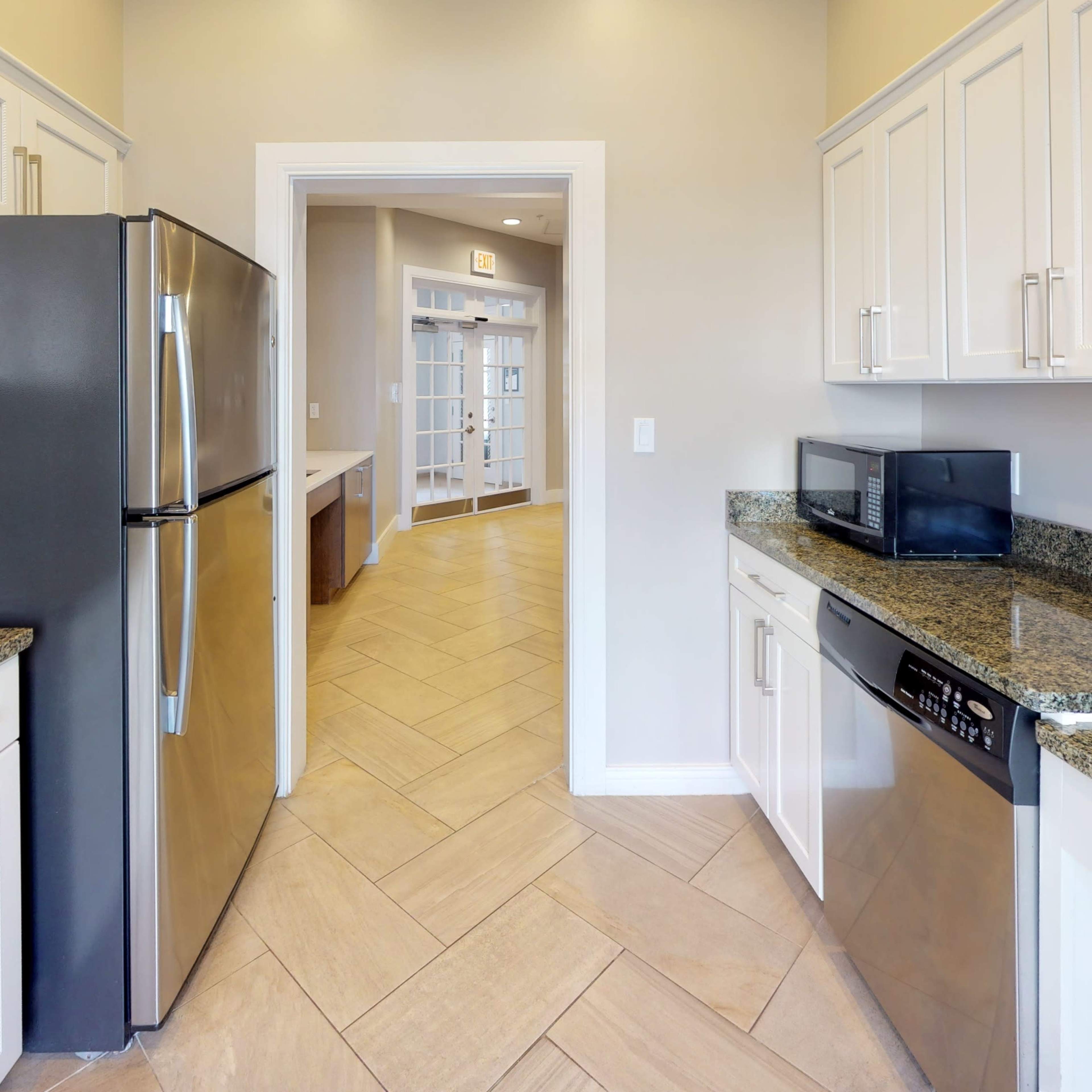A kitchen with stainless steel appliances, granite countertops, and tile flooring, leading to a doorway that opens into a bright, spacious area.