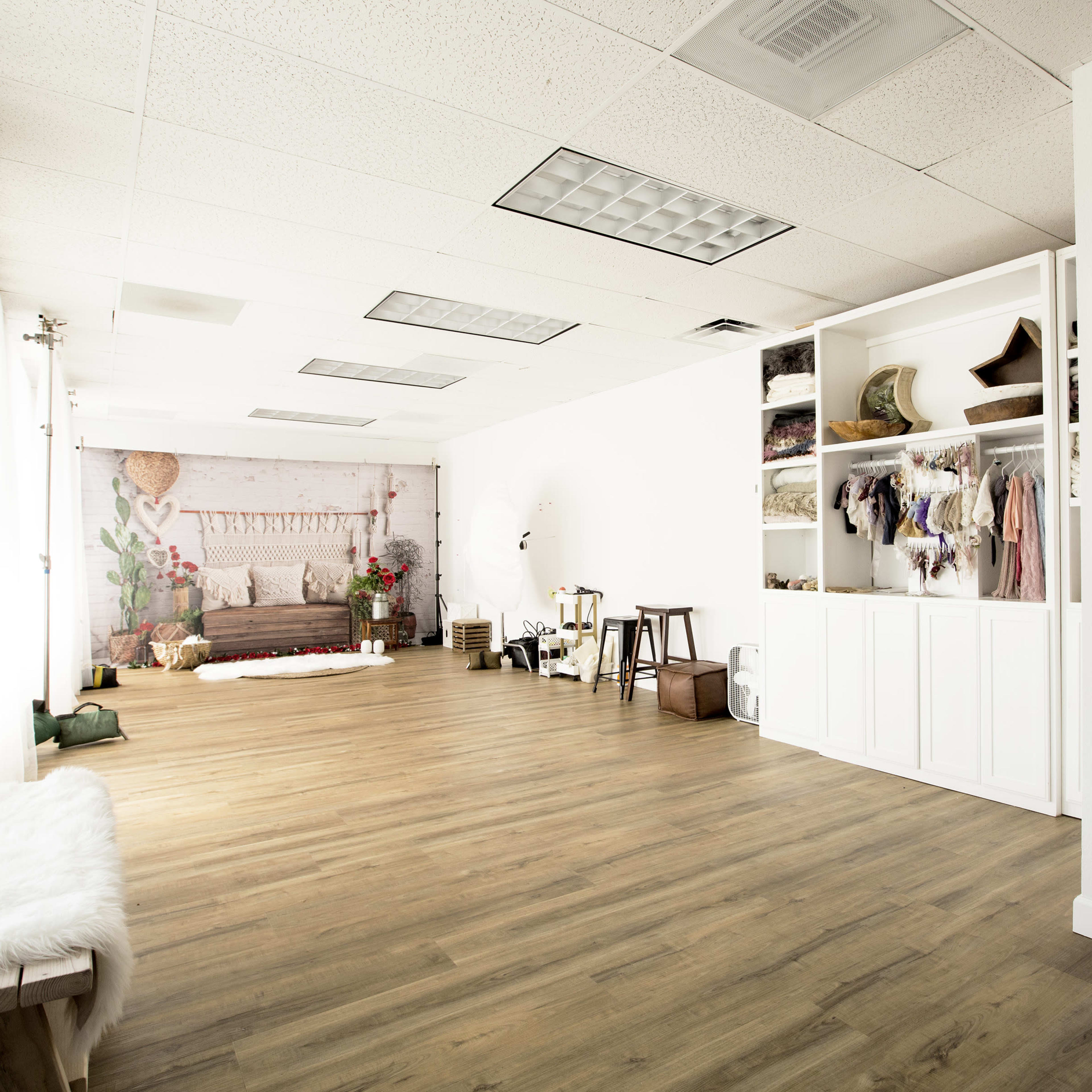 A spacious, well-lit studio with a wooden floor, showcasing a seating area, storage shelves, and a large mirror along the wall.