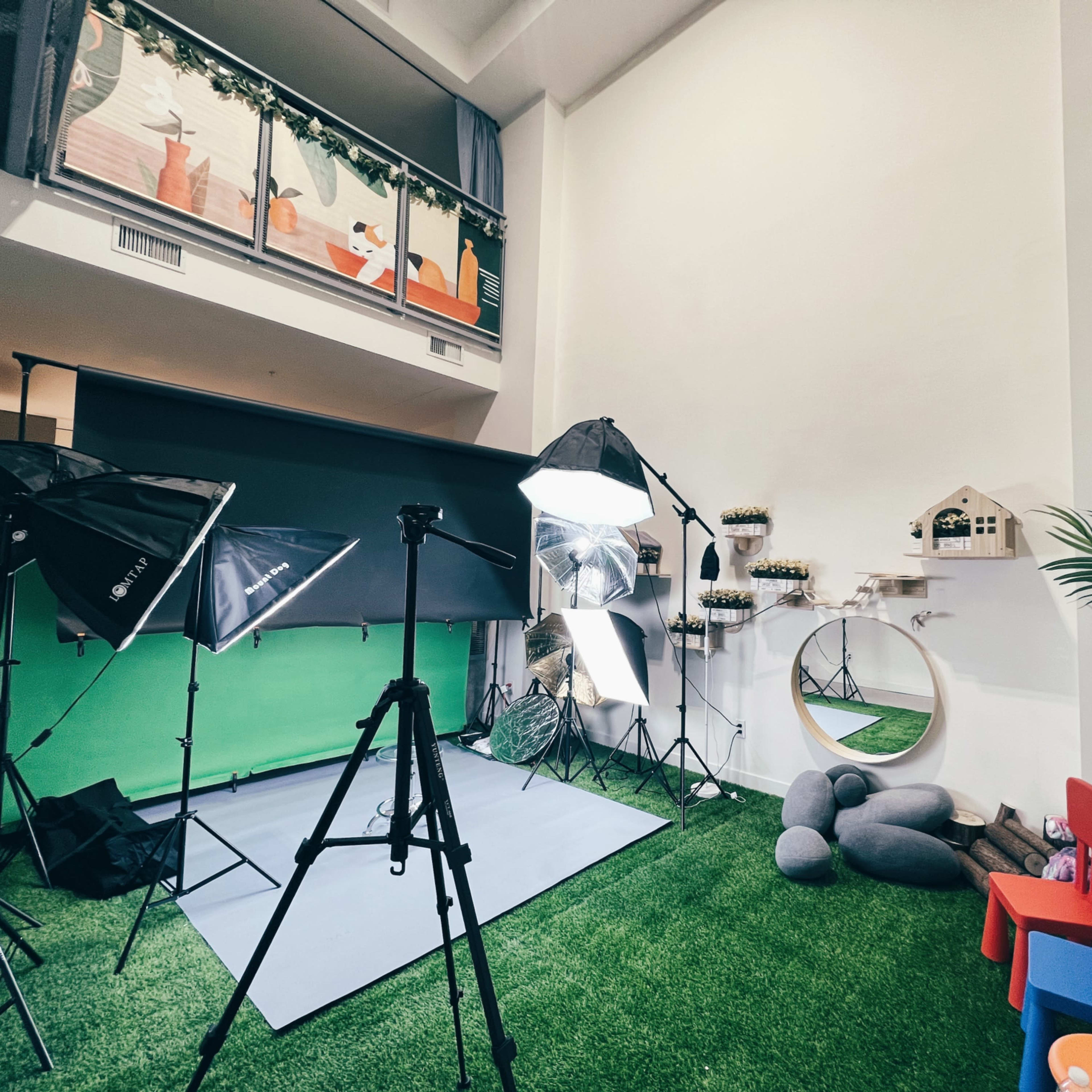 A photography studio setup with lighting equipment, a green screen backdrop, and a small play area with chairs and decorative items.