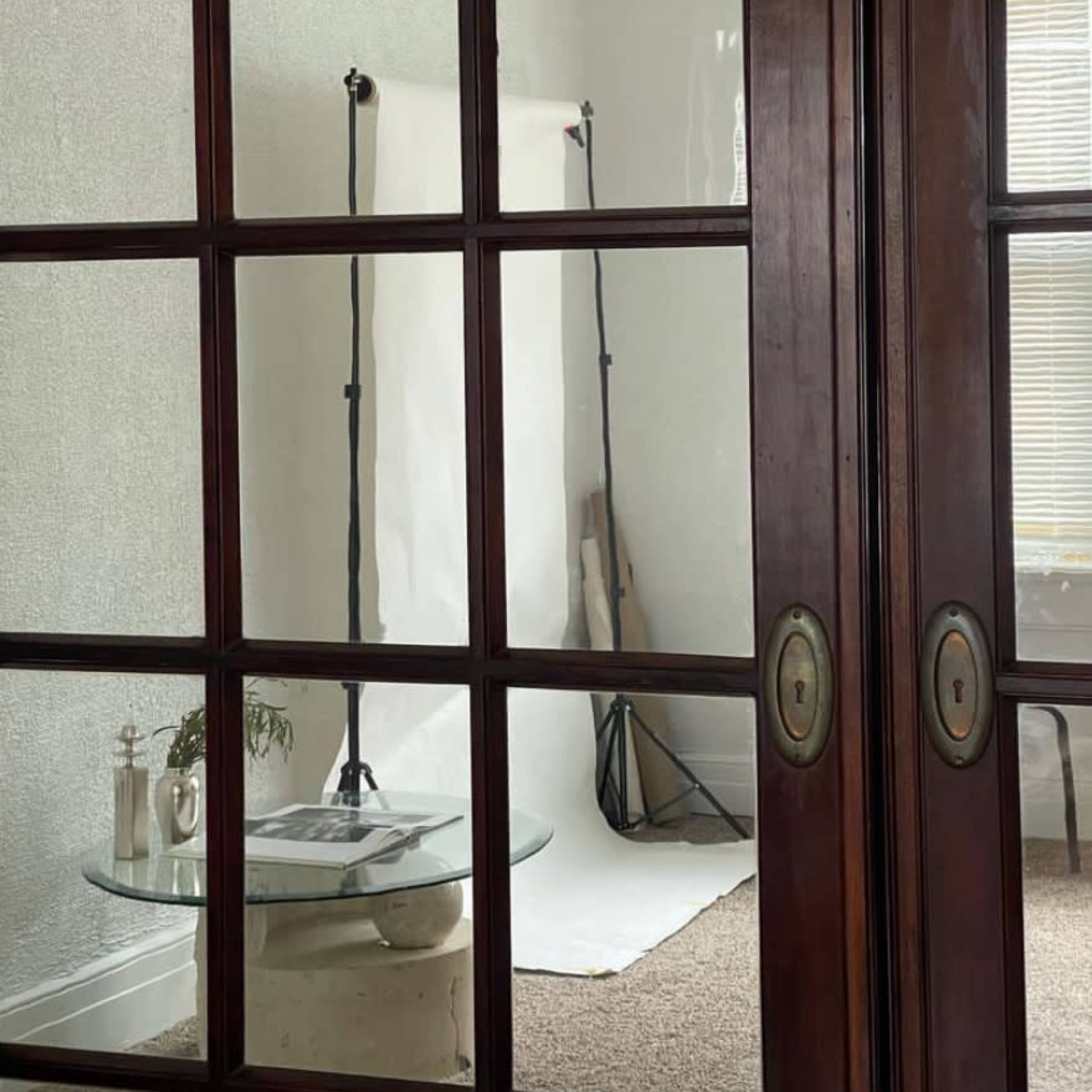 The scene shows a partitioned room with glass doors, revealing a minimalist setup featuring a backdrop and lighting stands on a light-colored floor.
