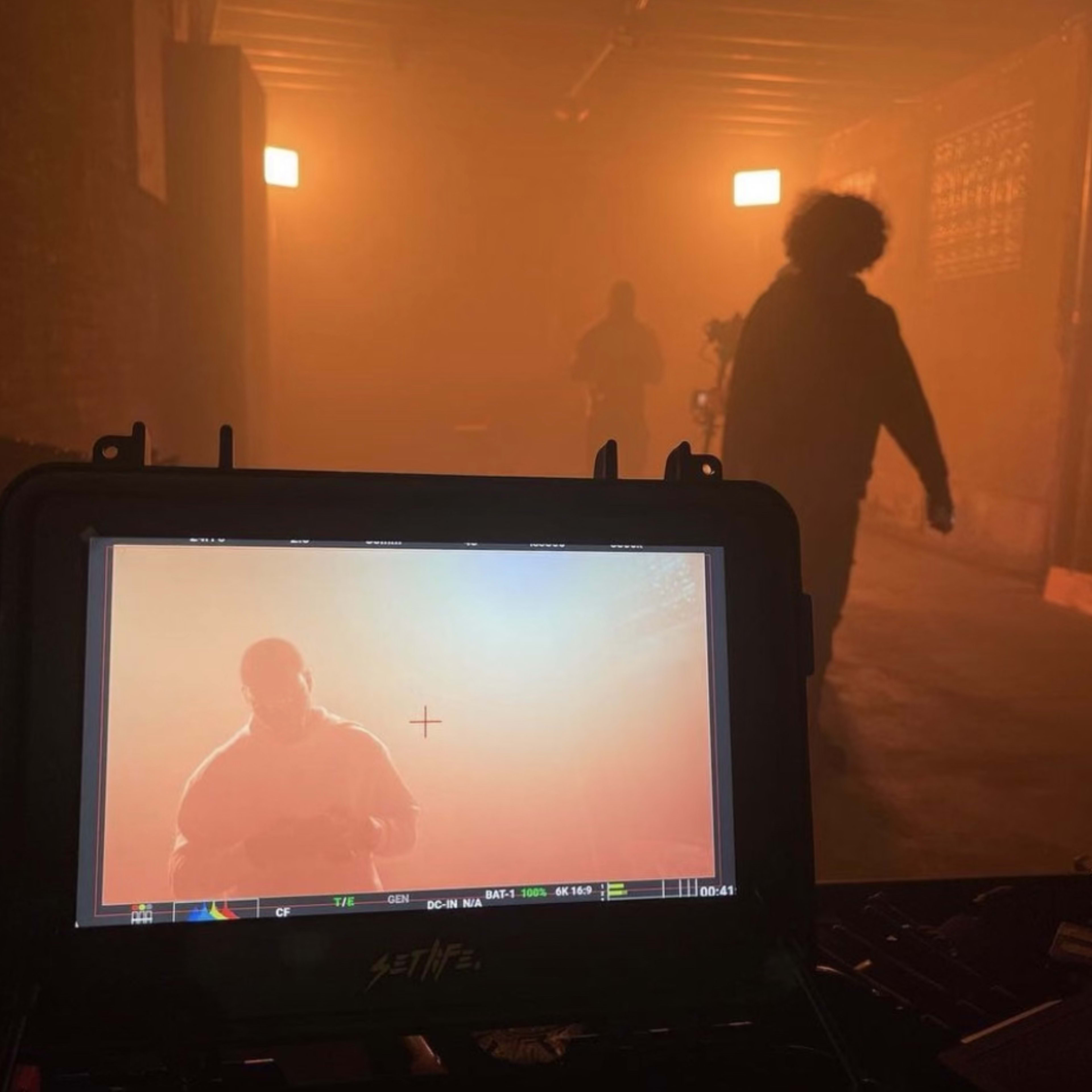 A monitor displays a hazy image of a figure in a dimly lit space with people moving in the background.