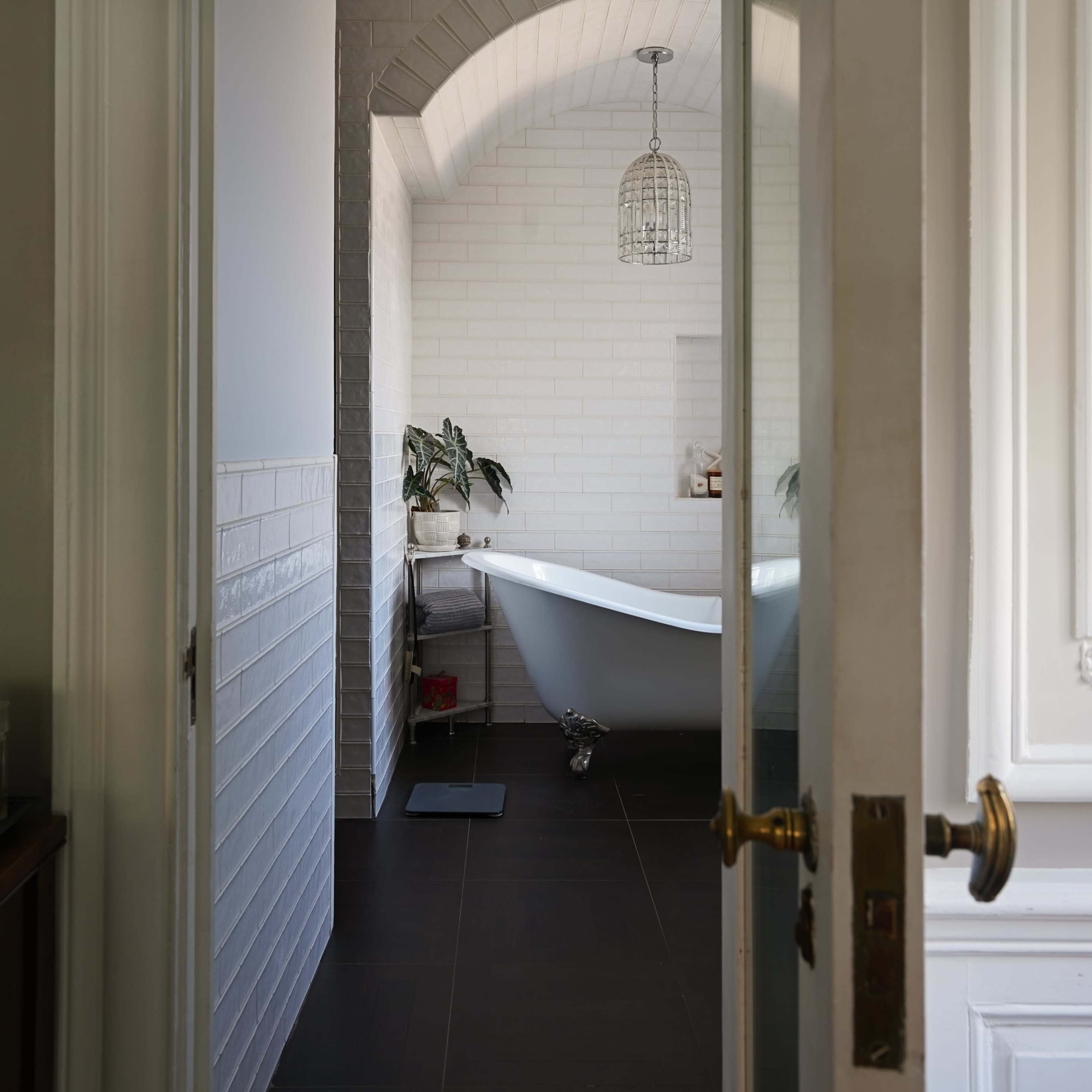 A doorway is seen leading to a bathroom featuring a freestanding bathtub, white brick walls, and a pendant light.