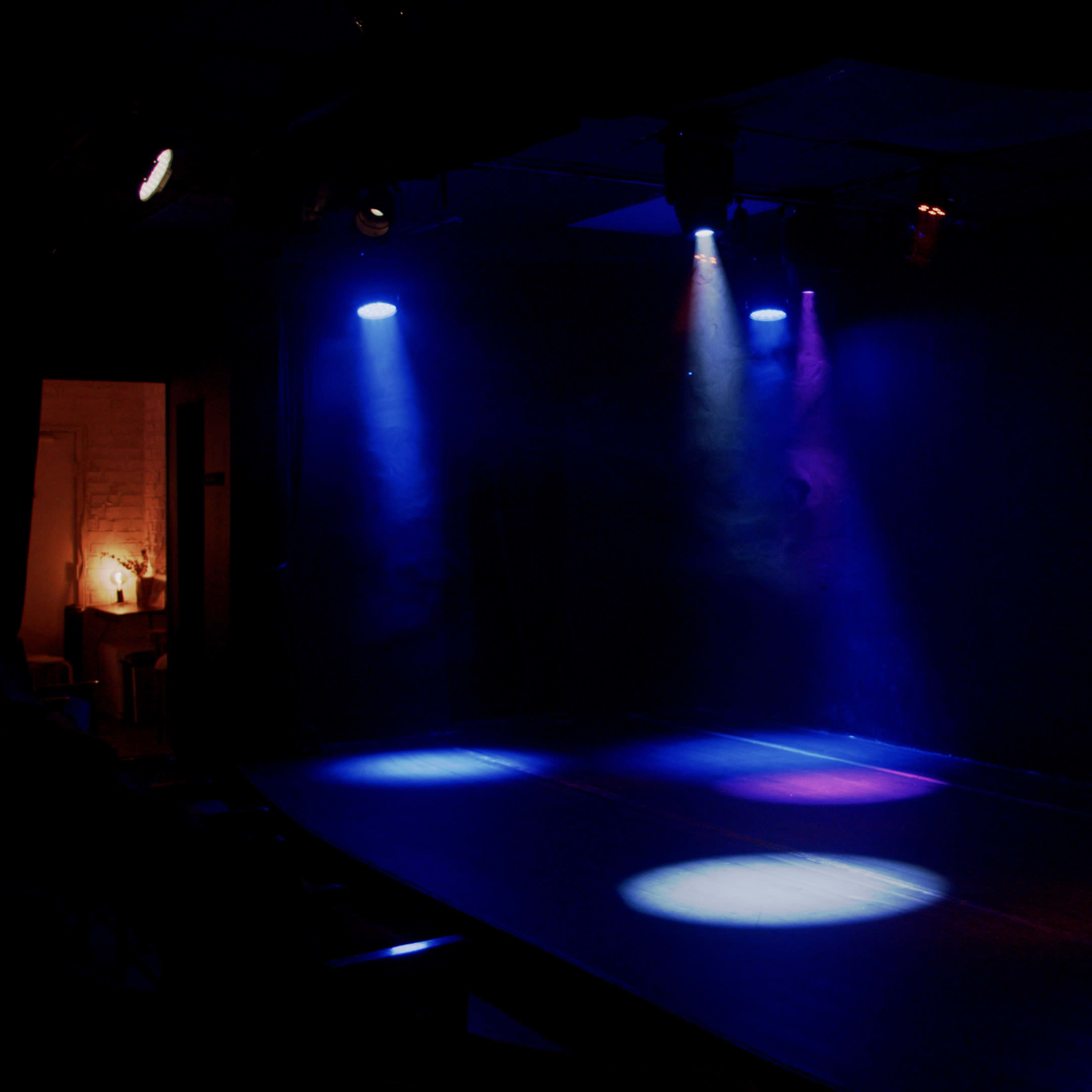 A dimly lit stage with blue and purple spotlight beams illuminating circular patches on the floor.