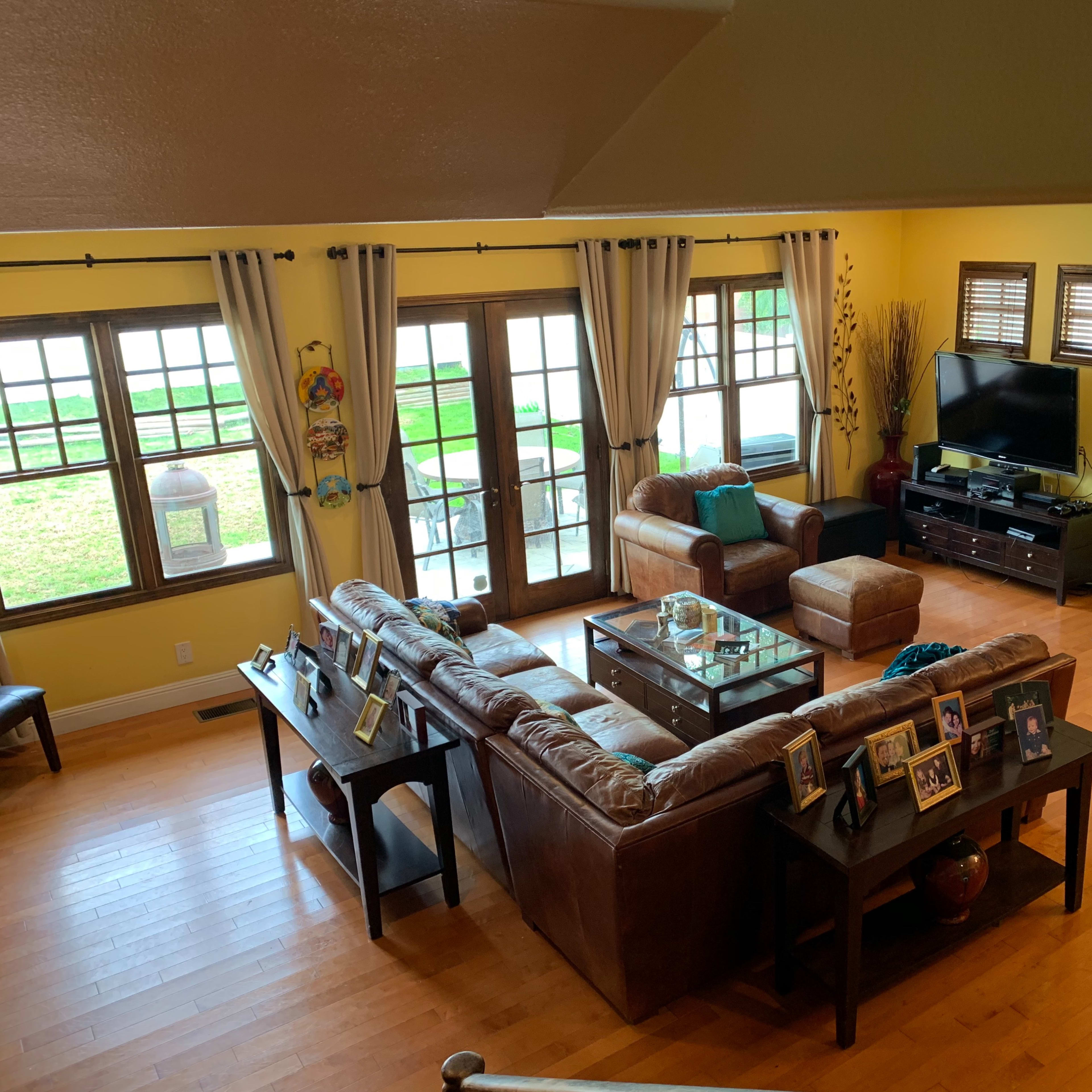A spacious living room with a brown leather sectional sofa, a coffee table, and large windows overlooking a grassy area.