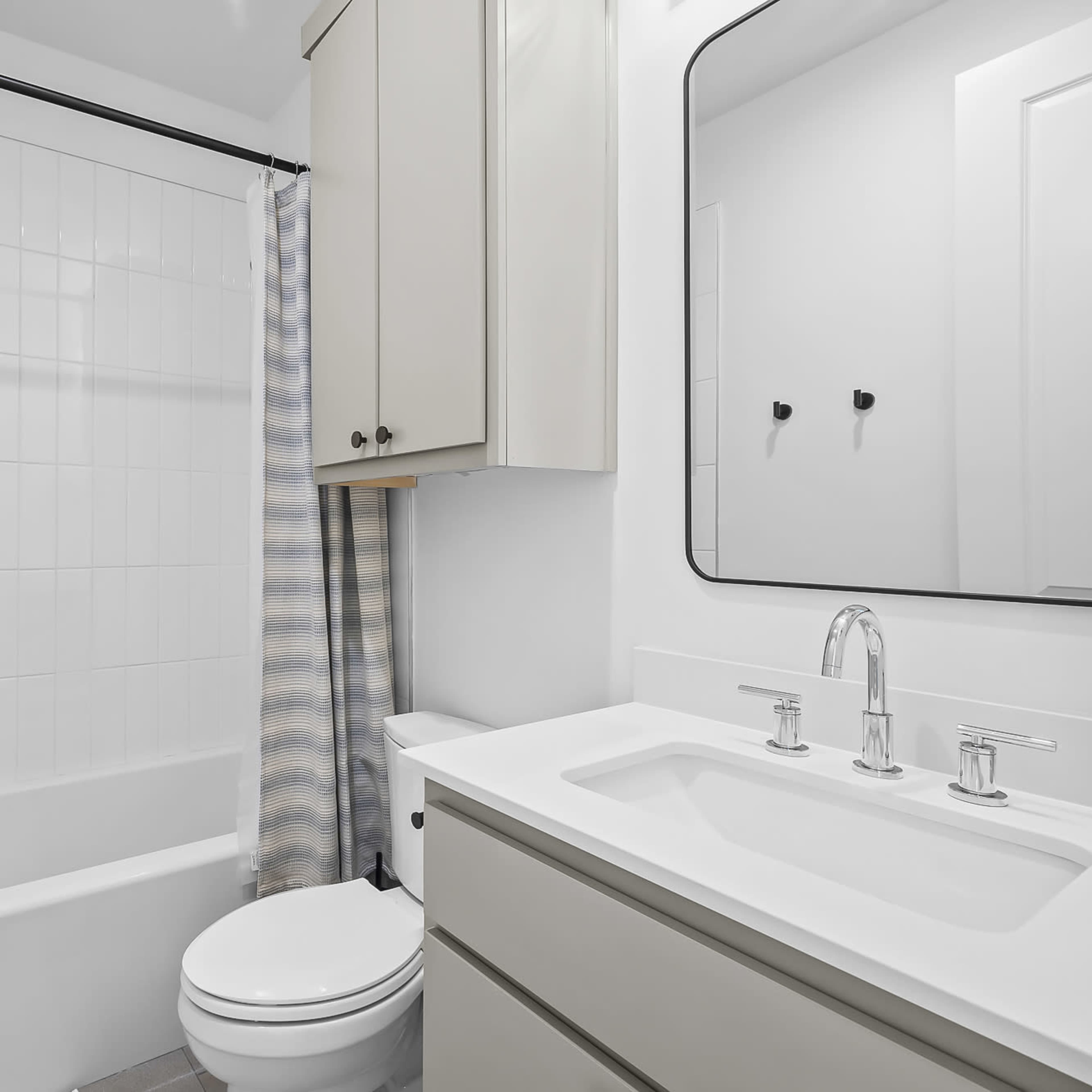 A modern bathroom featuring a bathtub with a shower curtain, a vanity with a sink and mirror, and light-colored cabinetry.