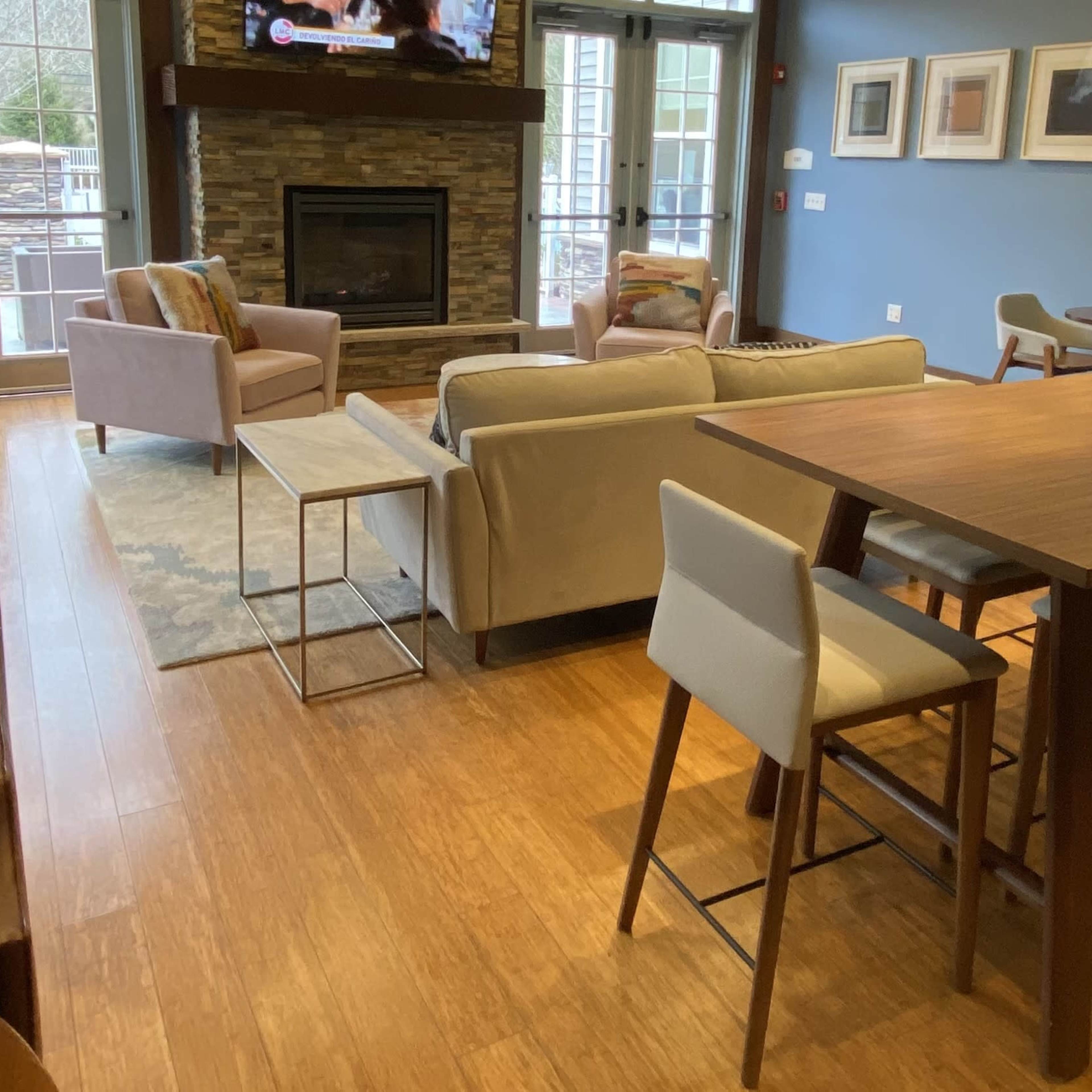A cozy lounge area featuring a fireplace, a dining table, and various seating arrangements, all set in a well-lit space with large windows.