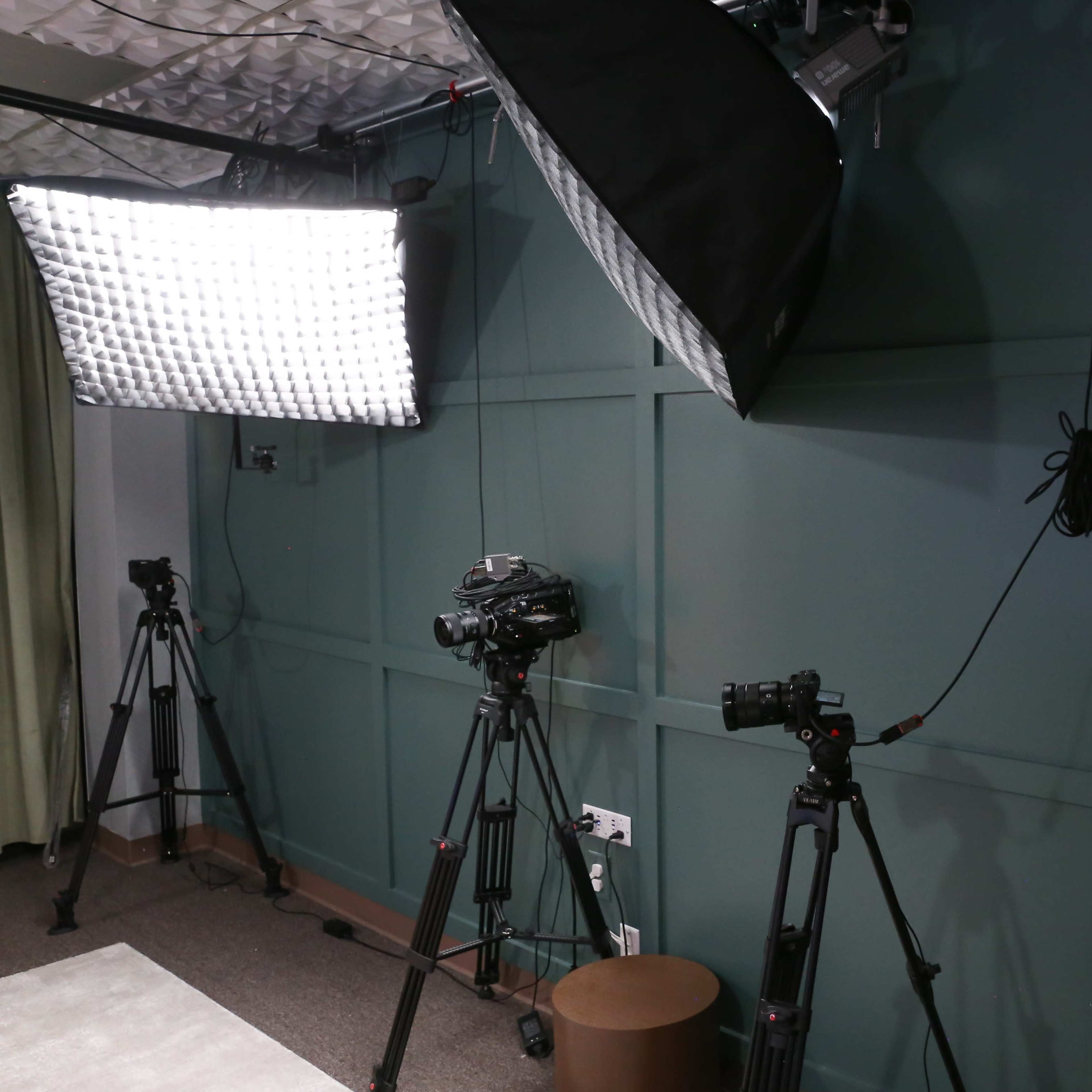 A corner of a studio with three cameras on tripods and a large softbox light mounted above.