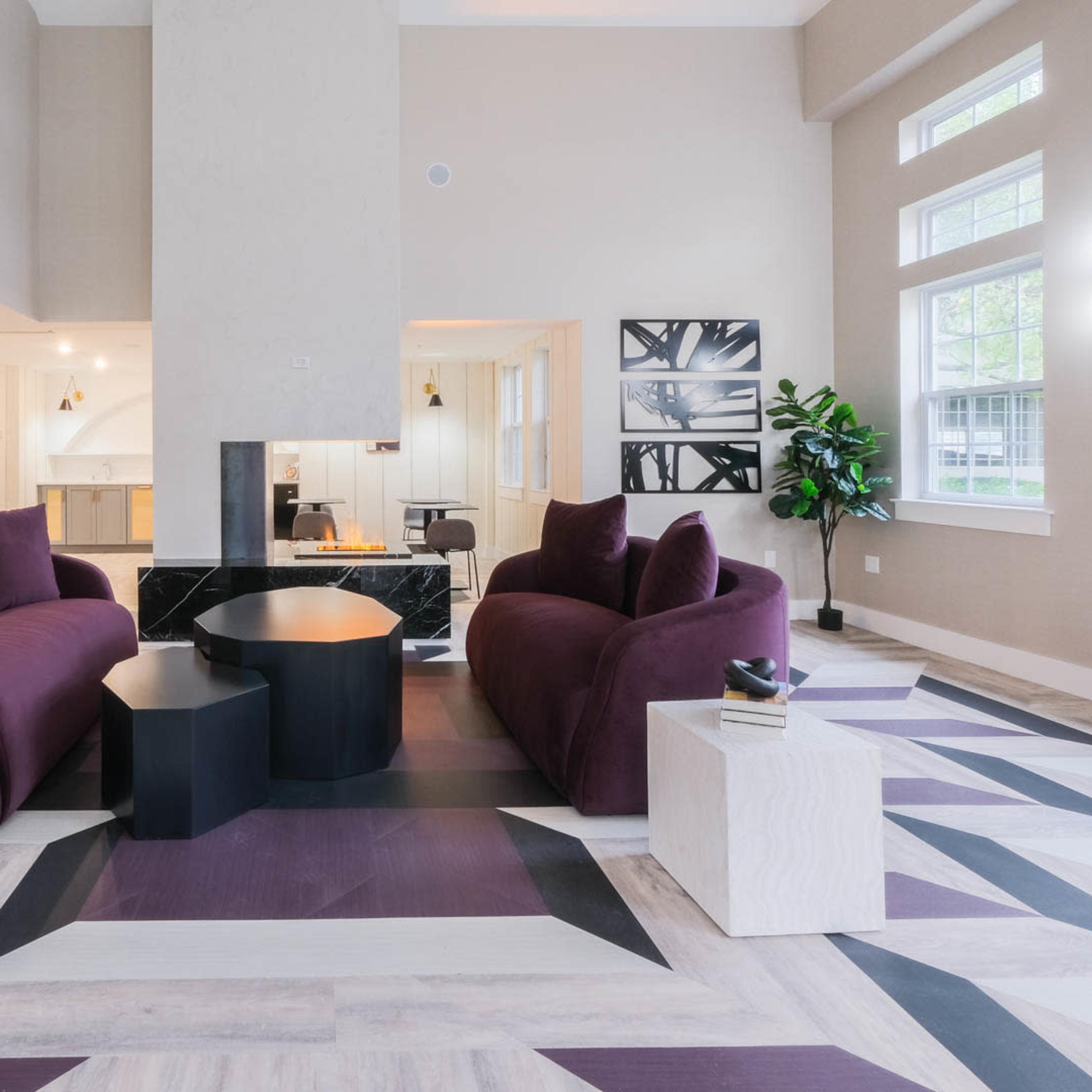 A modern lounge area featuring two purple sofas, a round coffee table, and a geometric patterned floor.