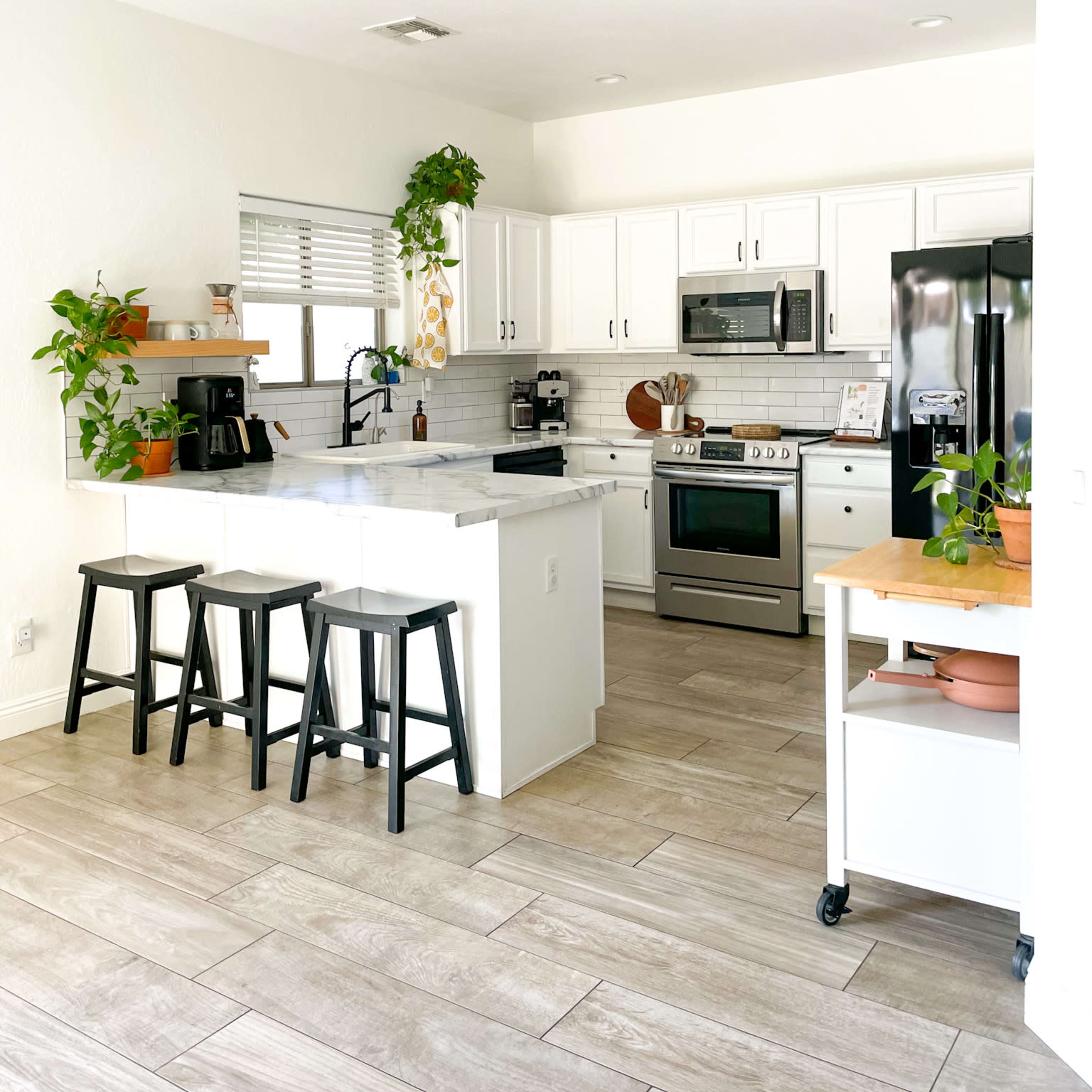 A modern kitchen with white cabinets, stainless steel appliances, and a wooden island with three black stools.