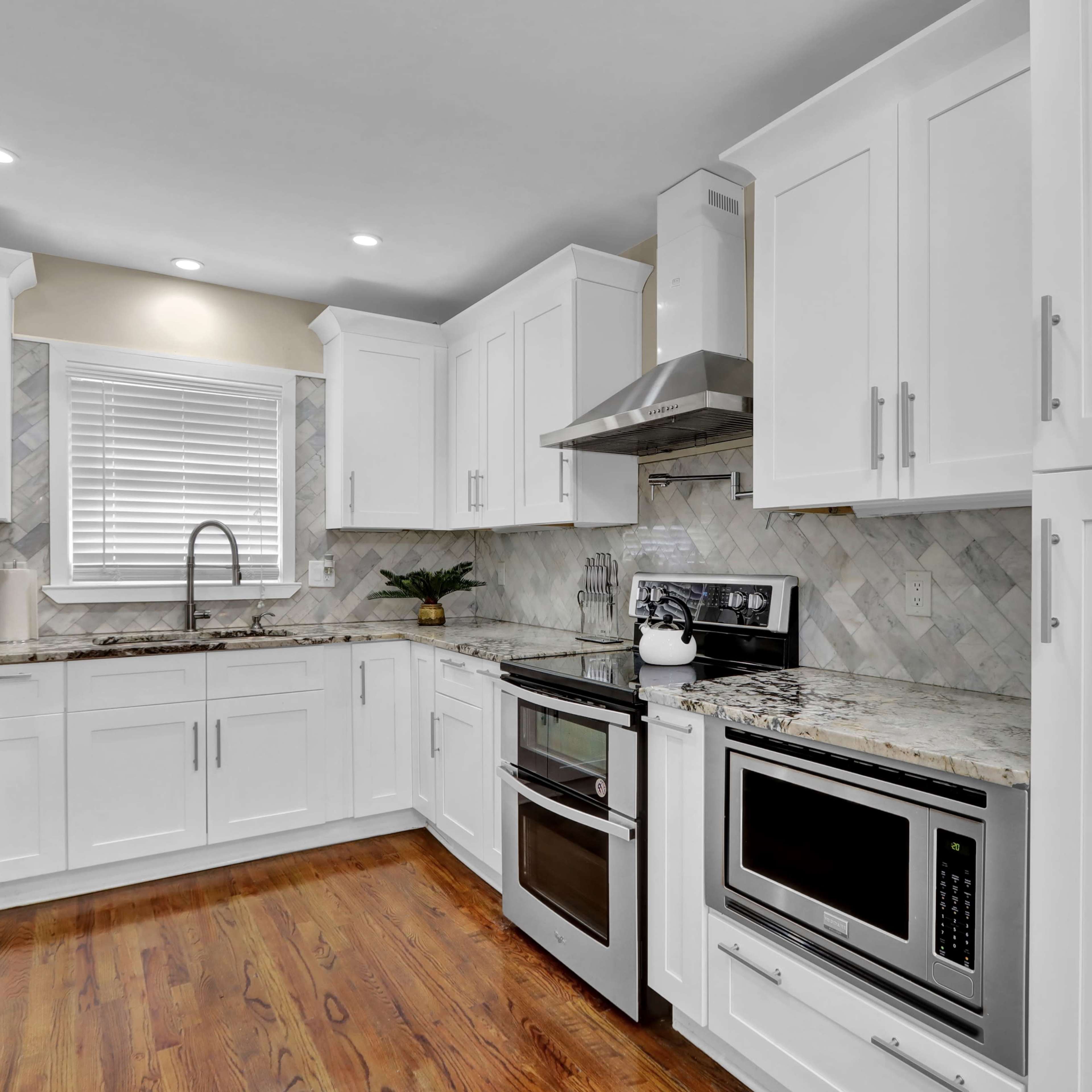 A modern kitchen features white cabinetry, stainless steel appliances, and a granite countertop with a herringbone backsplash.